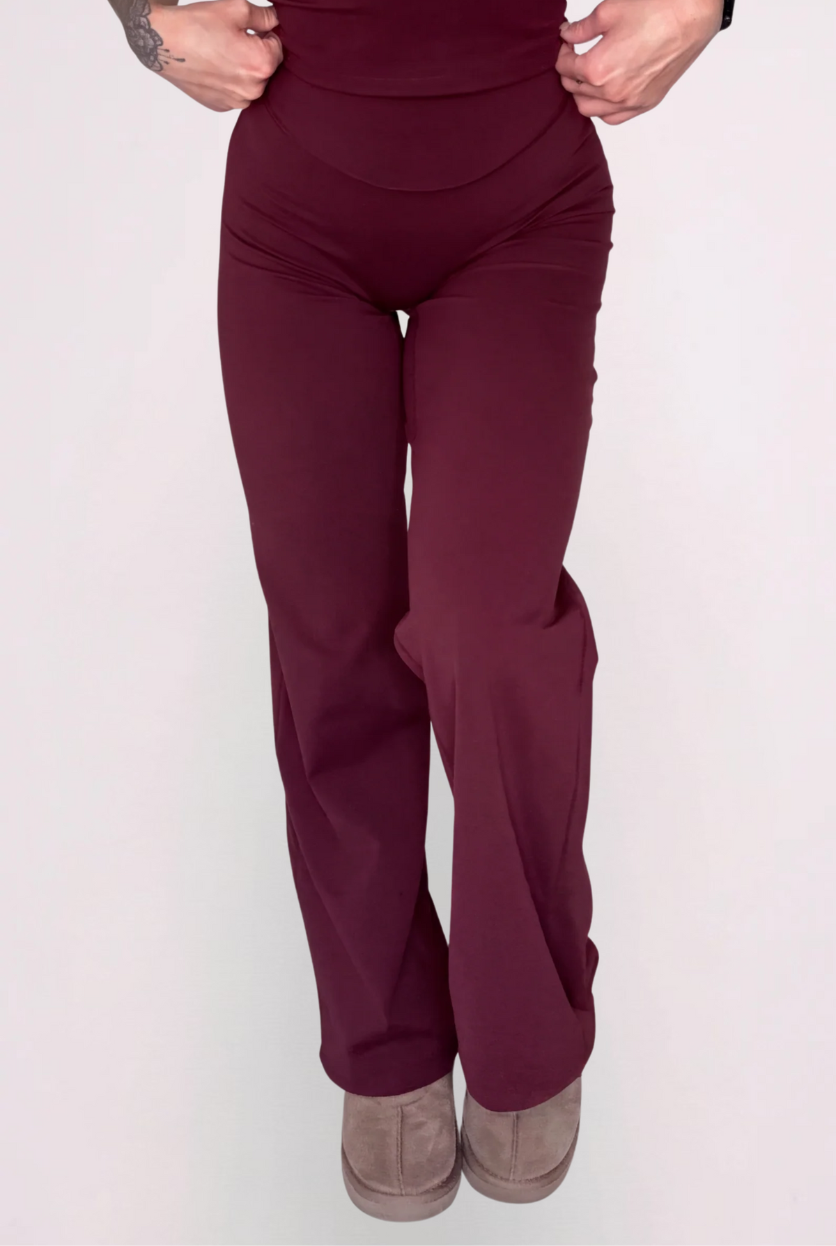 A model wearing a matching wine two-piece set consisting of a spaghetti-strap camisole top and high-waisted wide-leg pants, shown against a solid light grey background.