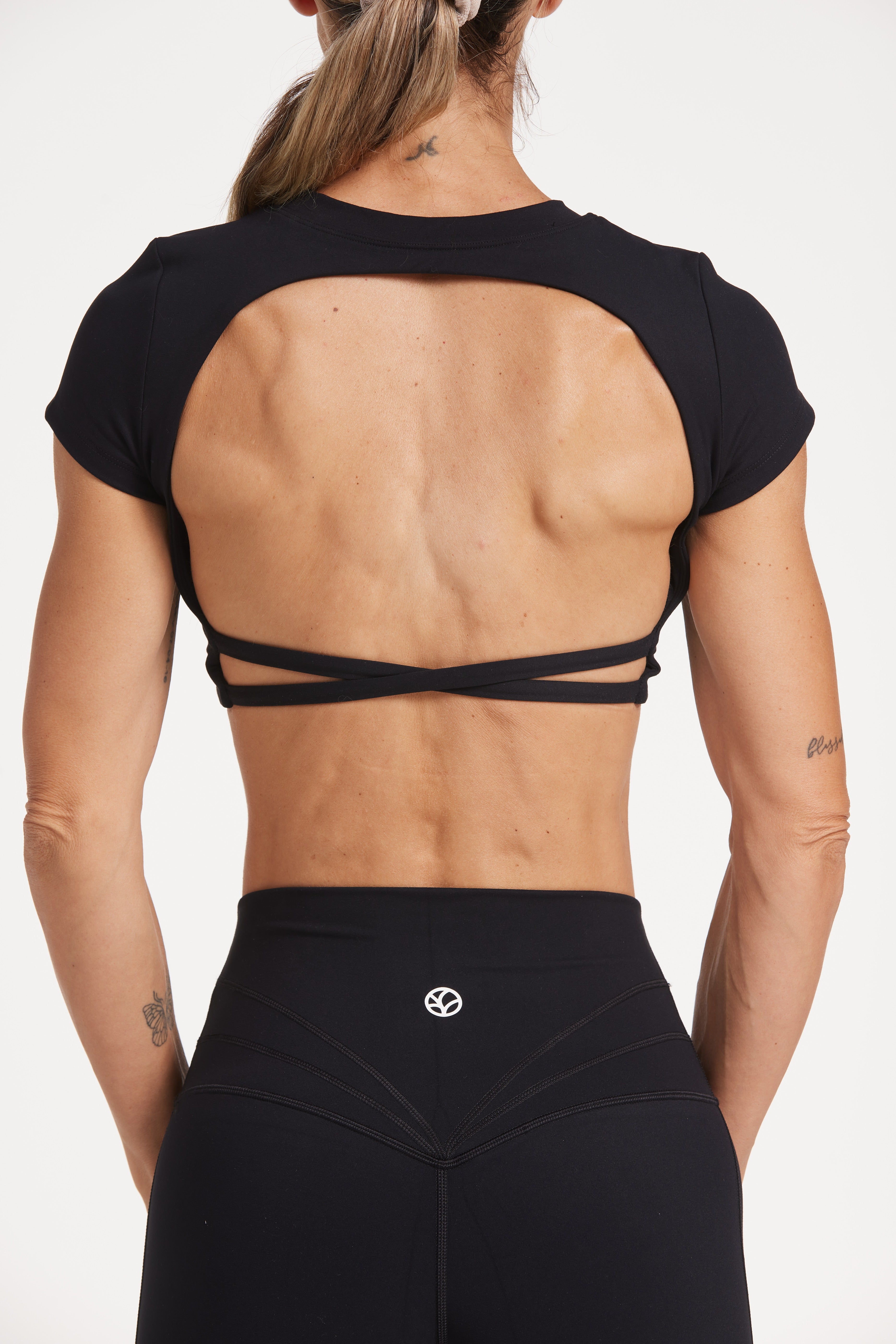 Buttery soft high waisted women's gym tights with curved hem stitched detailing for a butt shaping effect, and no front rise seam, paired with an open back women's crop t-shirt with a supportive elasticated hem and triple layered fabric with removable pads for extra support and aesthetic cross back straps in Black.