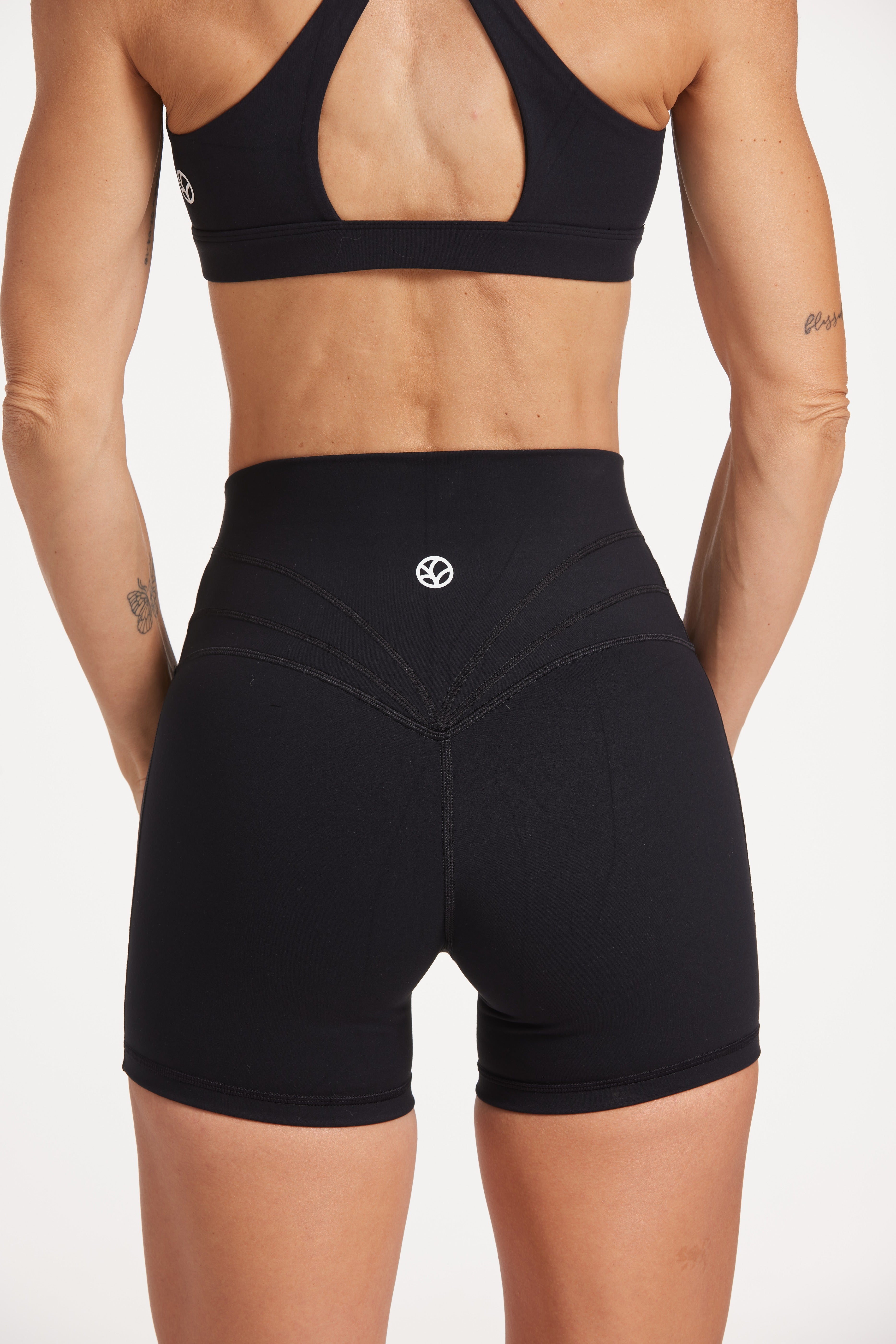 Buttery soft high waisted women's gym shorts with 4" inseam with curved stitched detailing for a butt shaping effect, and no front rise seam, paired with a high neck women's sports bra with a supportive elasticated hem and triple layered fabric with removable pads for extra support and crossover back straps in Black.