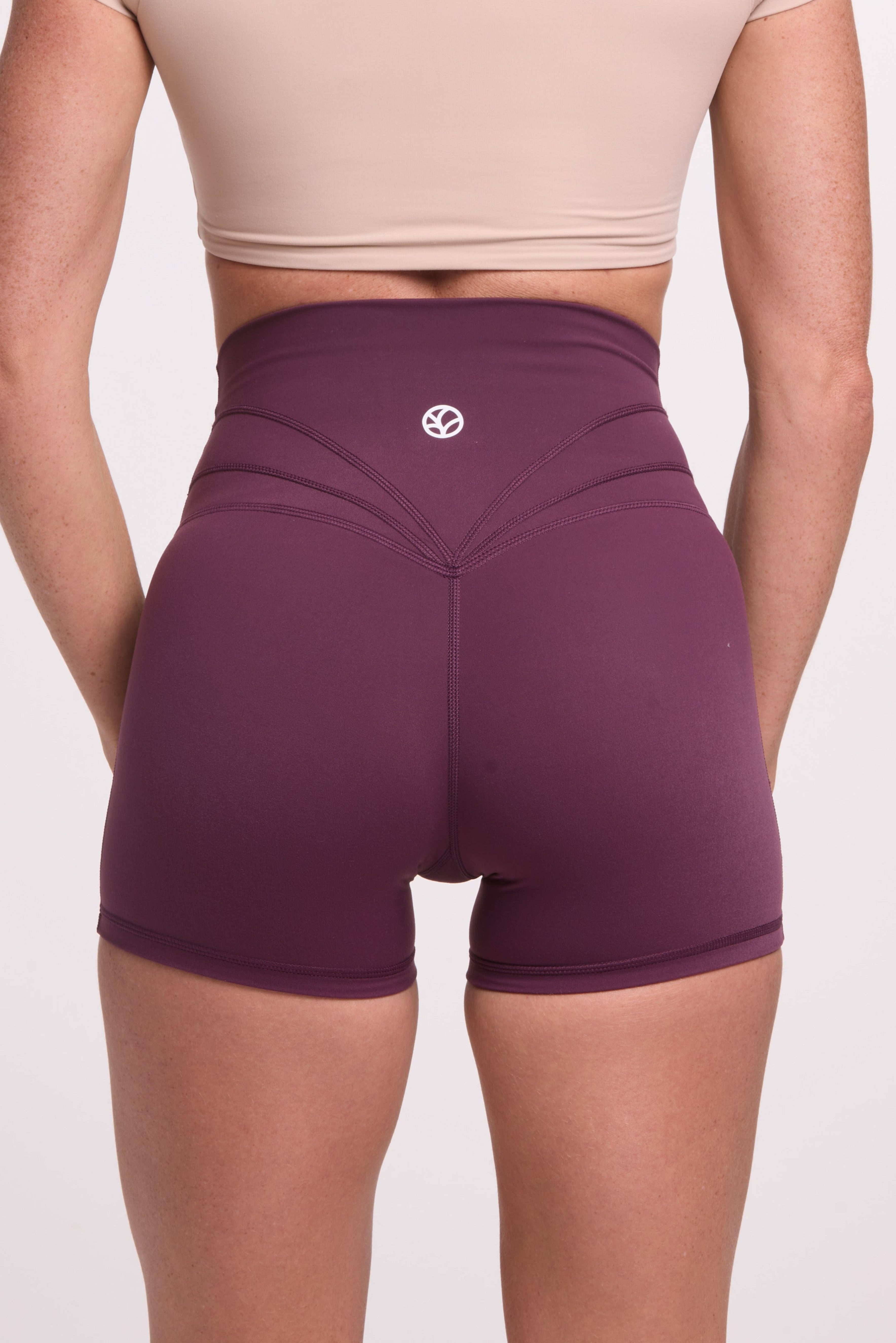 Buttery soft high waisted women's gym shorts with 4" inseam with curved stitched detailing for a butt shaping effect, and no front rise seam in plum purple paired with a V neck women's crop t-shirt with a supportive elasticated hem and triple layered fabric with removable pads for extra support in beige