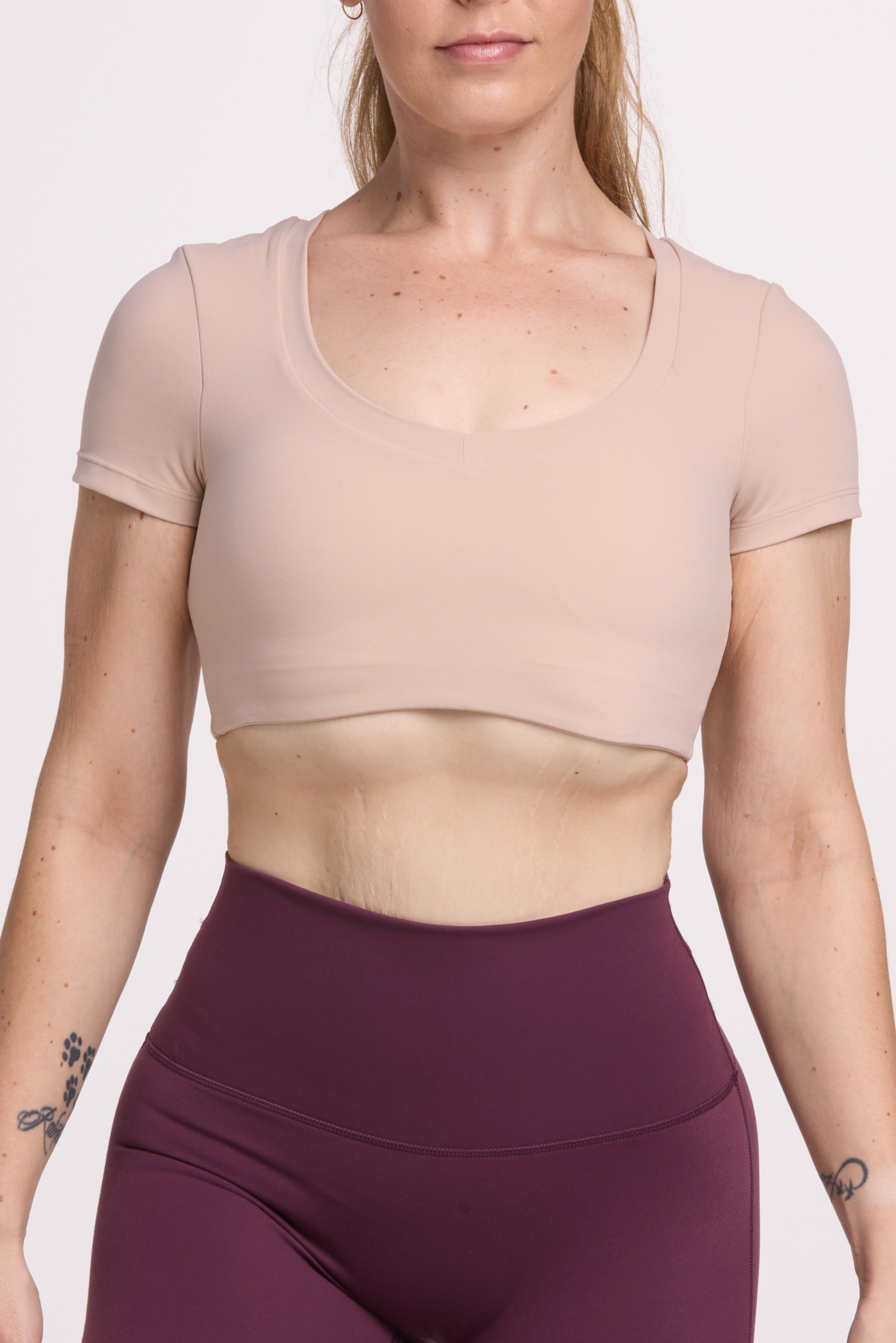 Buttery soft high waisted women's gym shorts with 4" inseam with curved stitched detailing for a butt shaping effect, and no front rise seam in mulberry wine paired with a V neck women's crop t-shirt with a supportive elasticated hem and triple layered fabric with removable pads for extra support in beige