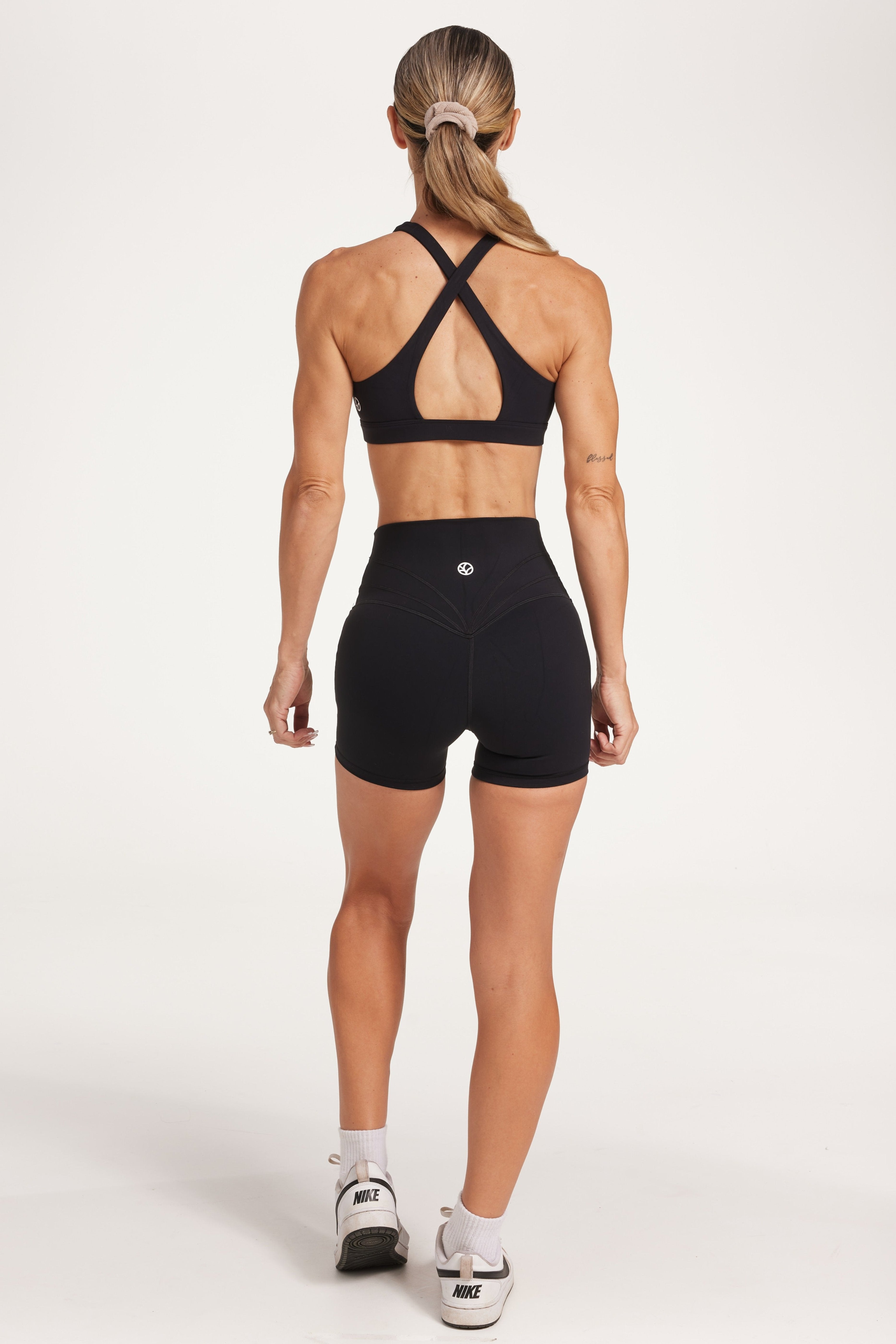 Buttery soft high waisted women's gym shorts with 4" inseam with curved stitched detailing for a butt shaping effect, and no front rise seam, paired with a high neck women's sports bra with a supportive elasticated hem and triple layered fabric with removable pads for extra support and crossover back straps in Black.