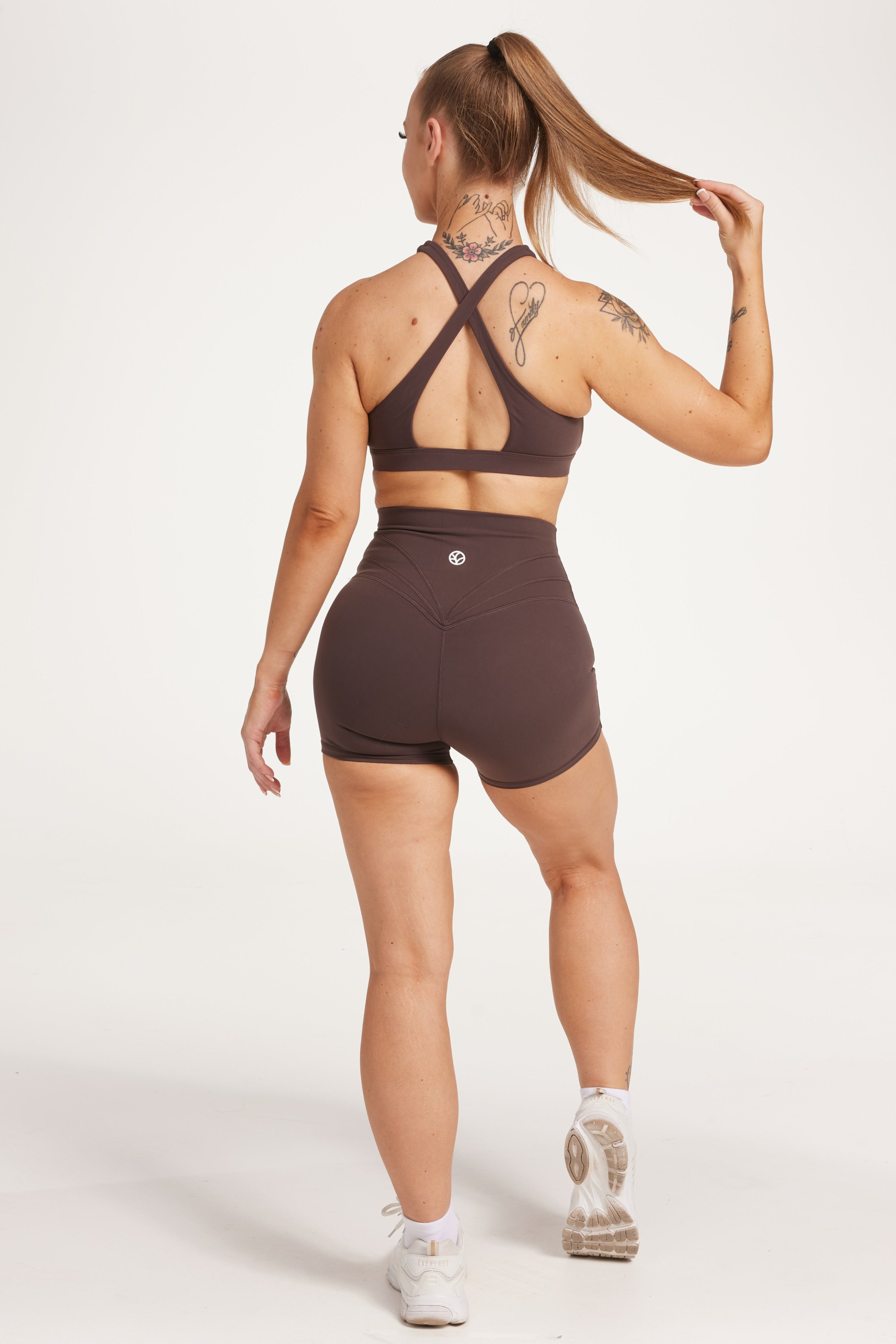 Buttery soft high waisted women's gym shorts with 4" inseam with curved stitched detailing for a butt shaping effect, and no front rise seam, paired with a high neck women's sports bra with a supportive elasticated hem and triple layered fabric with removable pads for extra support and crossover back straps in Dark Chocolate.