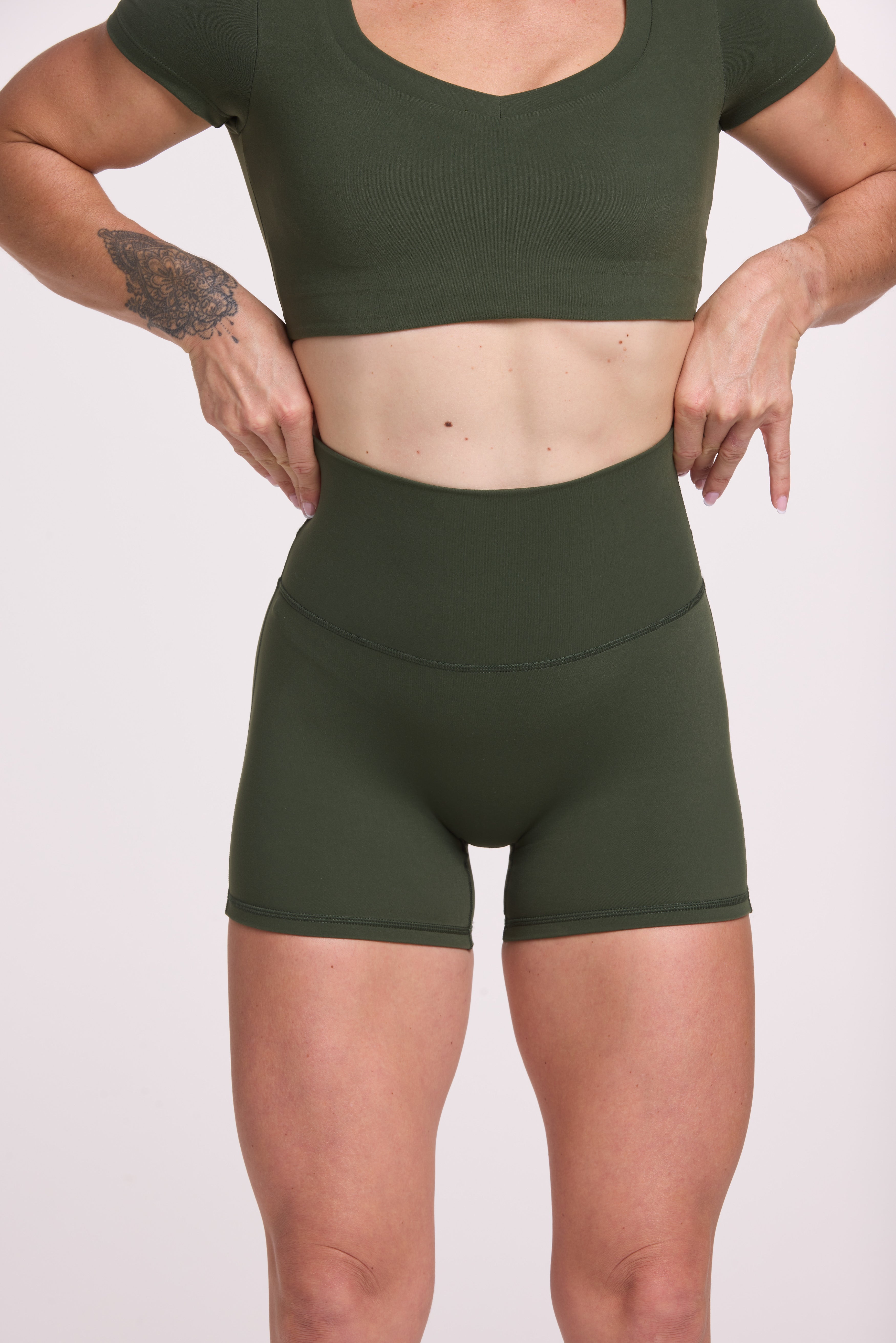 Buttery soft high waisted women's gym shorts with 4" inseam with curved stitched detailing for a butt shaping effect, and no front rise seam, paired with a V neck women's crop t-shirt with a supportive elasticated hem and triple layered fabric with removable pads for extra support in forest green