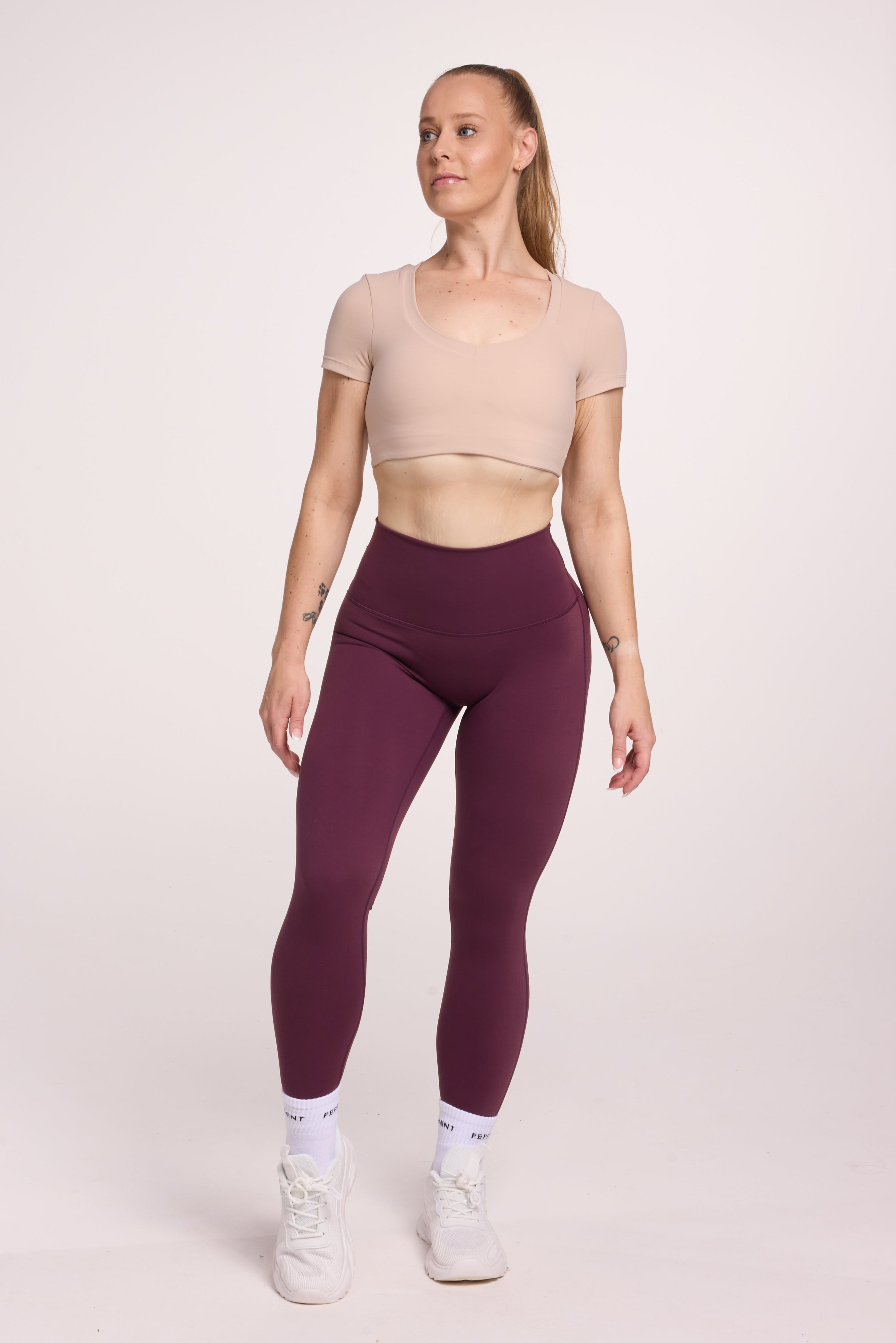 Buttery soft high waisted women's gym tights with curved back seam stitched detailing for a butt shaping effect, and no front rise seam, in plum purple paired with an V neck women's crop t-shirt with a supportive elasticated hem and triple layered fabric with removable pads for extra support in
beige