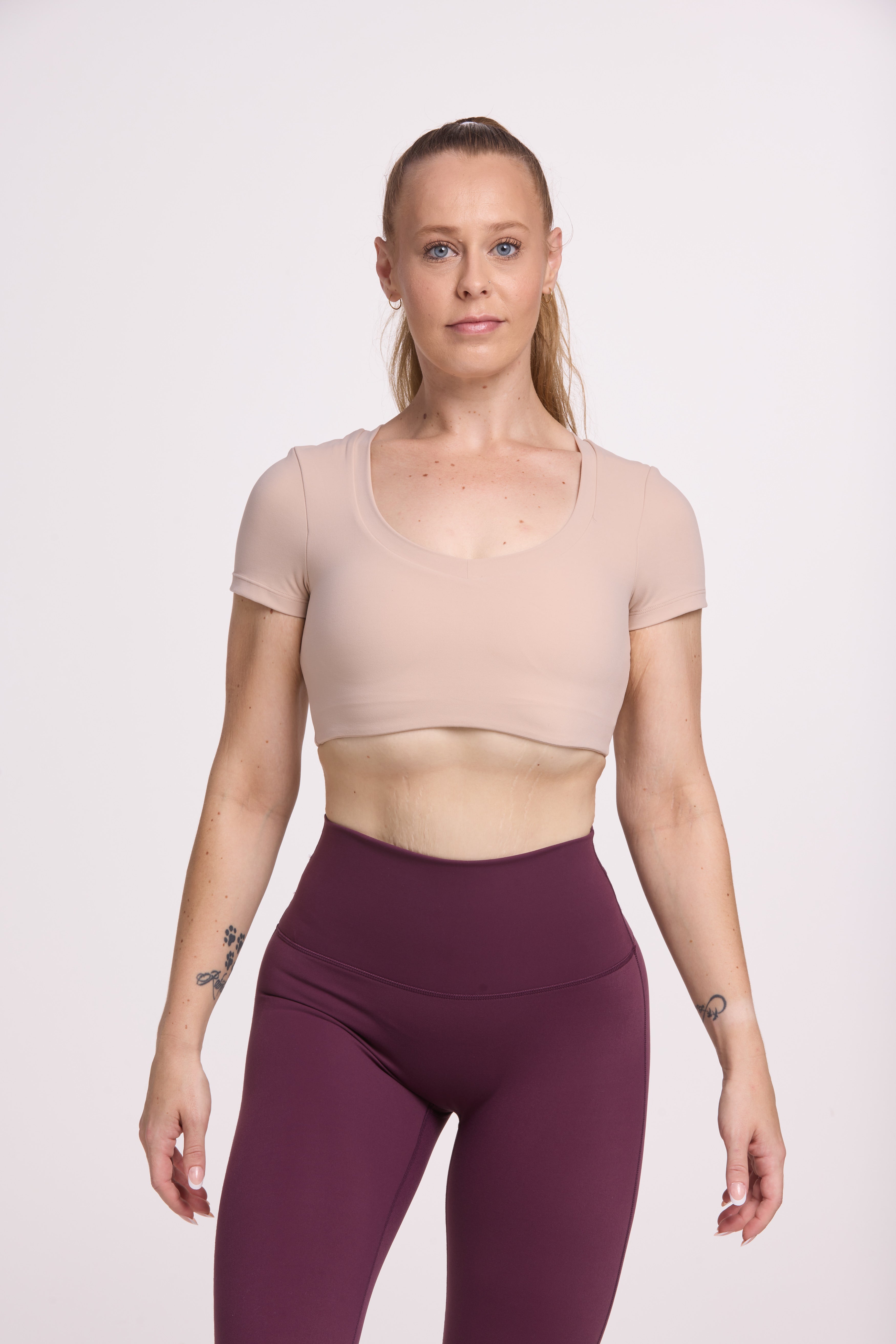 Buttery soft high waisted women's gym tights with curved back seam stitched detailing for a butt shaping effect, and no front rise seam, in plum purple paired with an V neck women's crop t-shirt with a supportive elasticated hem and triple layered fabric with removable pads for extra support in
beige
