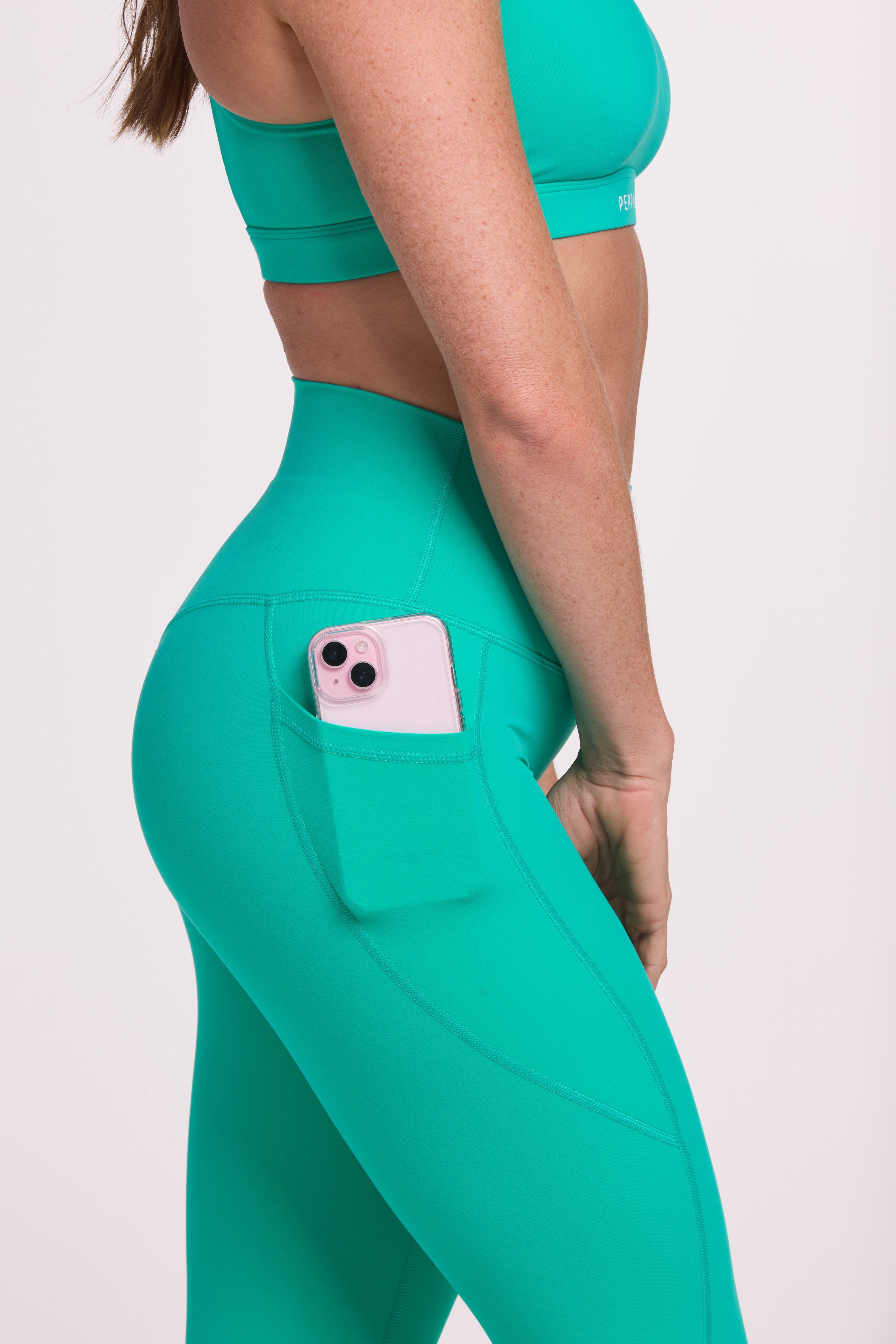 Buttery soft high waisted women's gym tights with practical pockets, sweetheart back seams for an upper glute shaping effect, and no front rise seam paired with a high neck women's sports bra with a supportive elasticated hem and triple layered fabric with removable pads for extra support and crossover back straps in cyan green