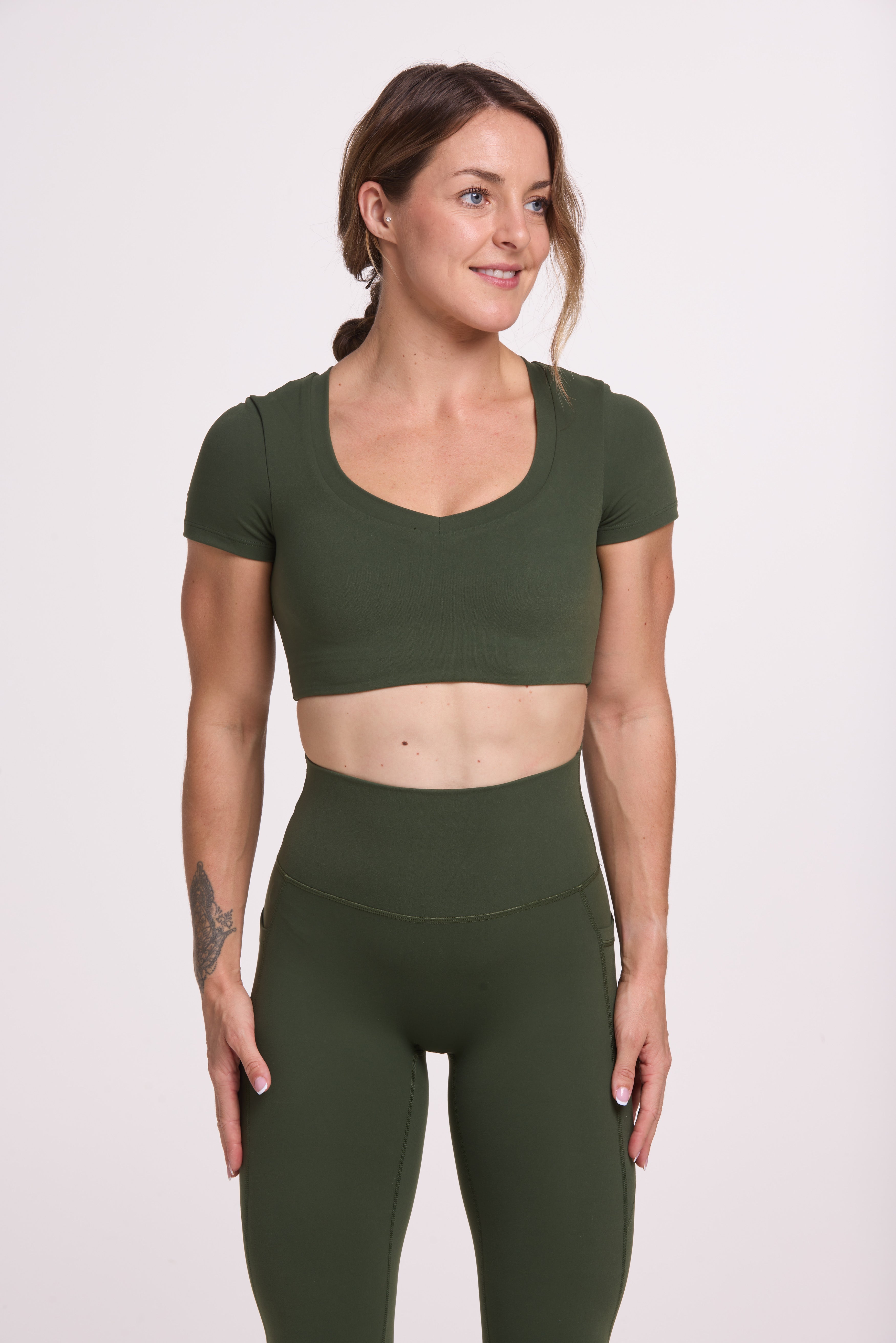 Buttery soft high waisted women's gym tights with practical pockets, sweetheart back seams for an upper glute shaping effect, and no front rise seam, paired with an V neck women's crop t-shirt with a supportive elasticated hem and triple layered fabric with removable pads for extra support in forest green