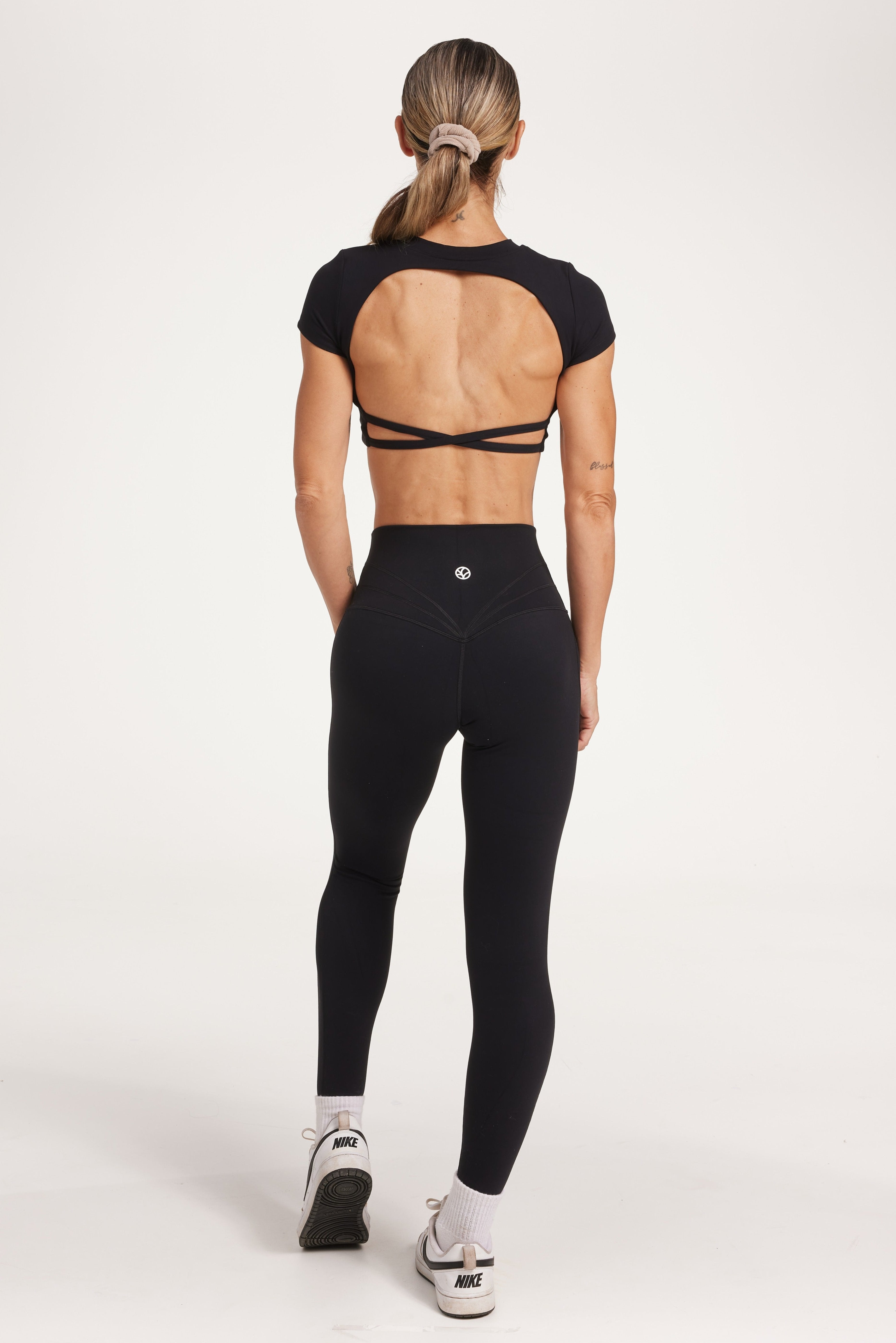 Buttery soft high waisted women's gym tights with curved hem stitched detailing for a butt shaping effect, and no front rise seam, paired with an open back women's crop t-shirt with a supportive elasticated hem and triple layered fabric with removable pads for extra support and aesthetic cross back straps in Black.