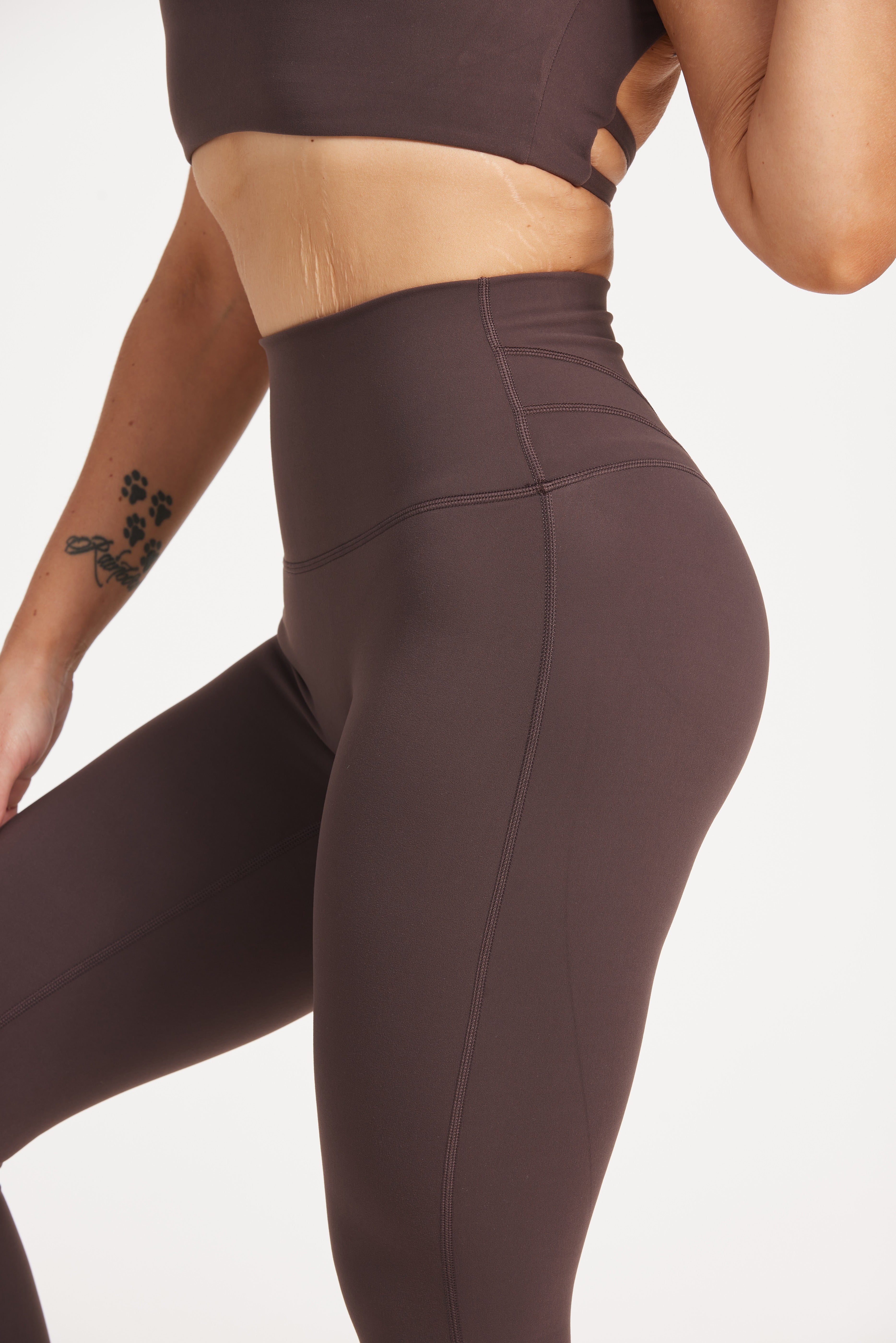 Buttery soft high waisted women's gym tights with curved hem stitched detailing for a butt shaping effect, and no front rise seam, paired with an open back women's crop t-shirt with a supportive elasticated hem and triple layered fabric with removable pads for extra support and aesthetic cross back straps in dark chocolate.
