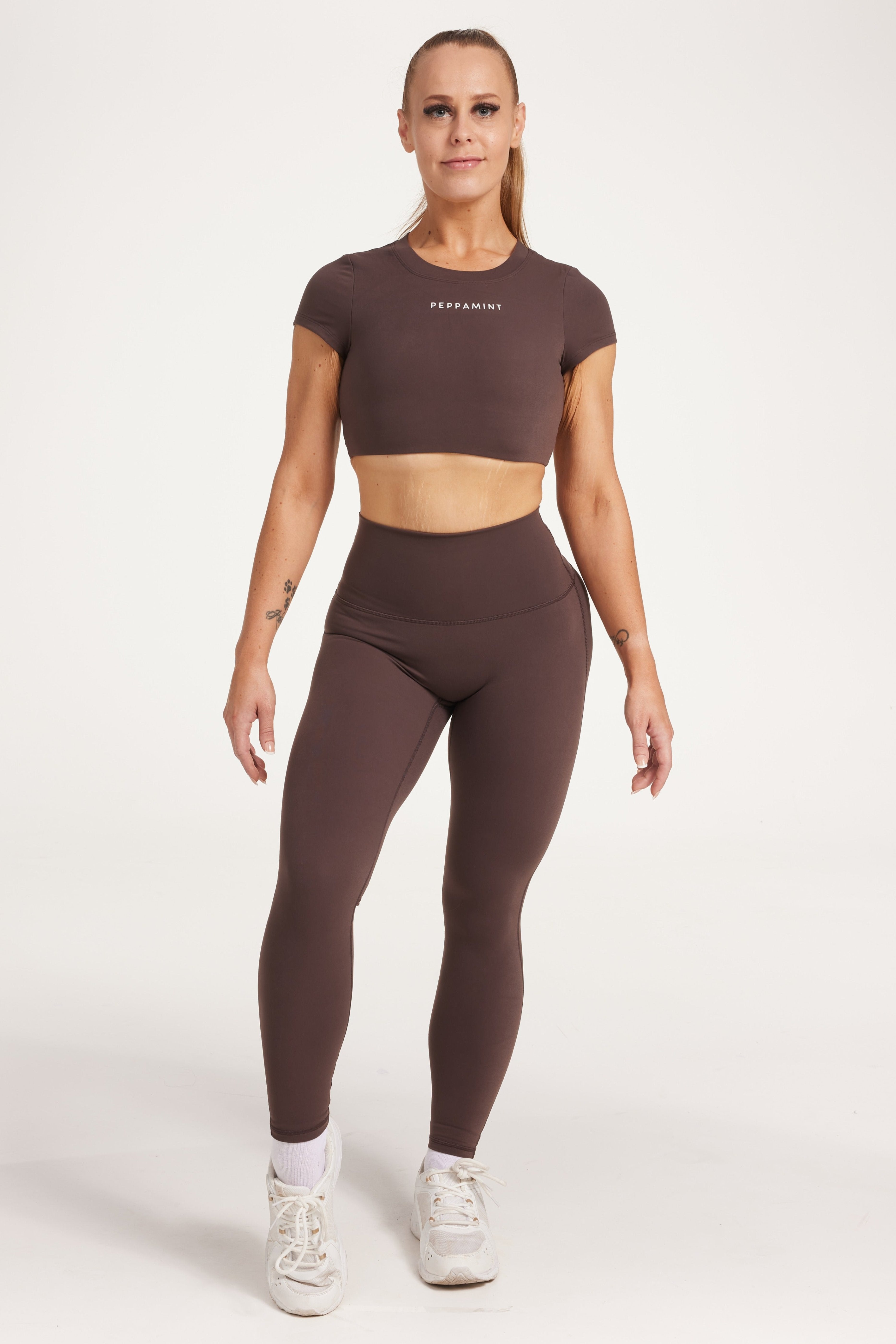 Buttery soft high waisted women's gym tights with curved hem stitched detailing for a butt shaping effect, and no front rise seam, paired with an open back women's crop t-shirt with a supportive elasticated hem and triple layered fabric with removable pads for extra support and aesthetic cross back straps in dark chocolate.