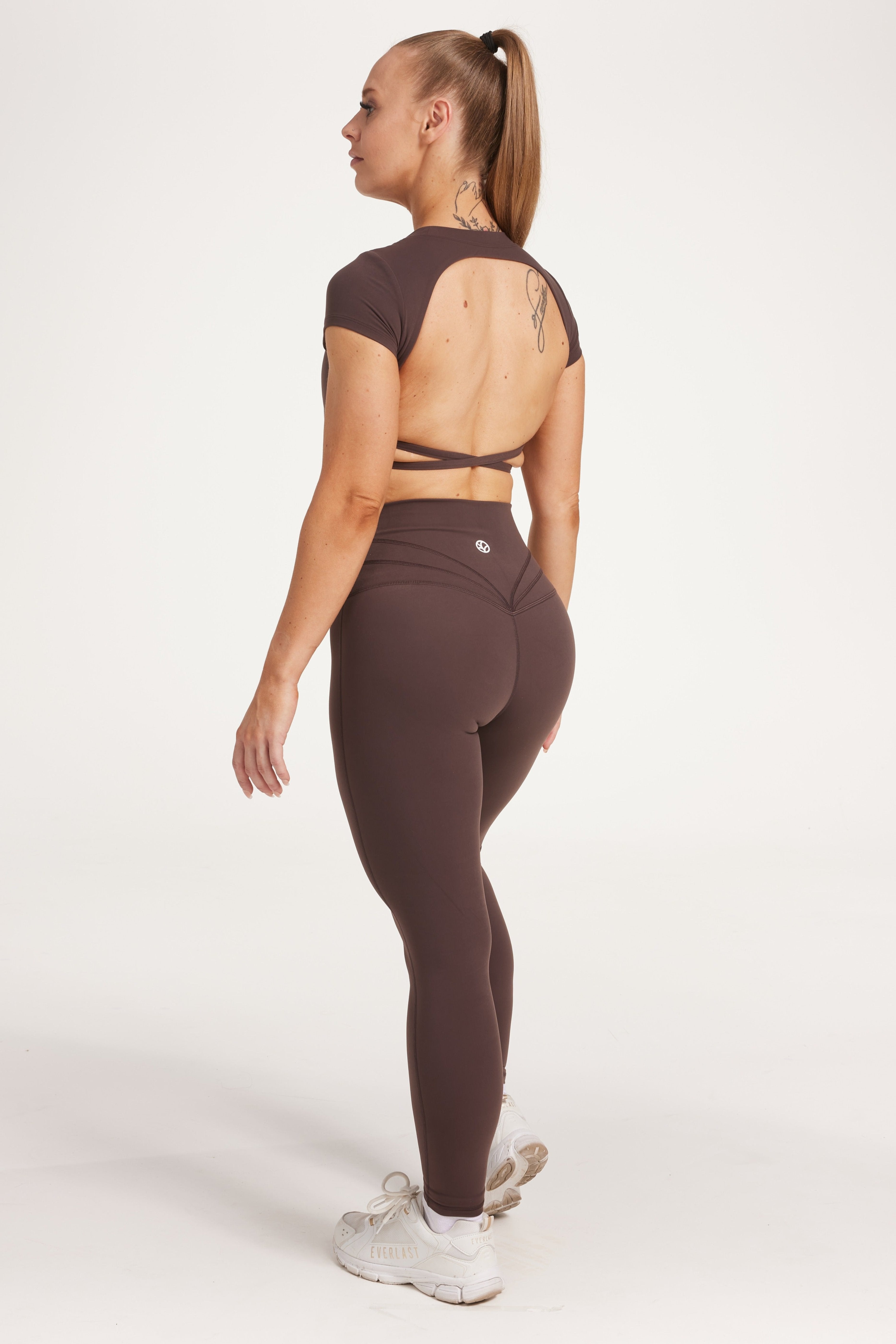 Buttery soft high waisted women's gym tights with curved hem stitched detailing for a butt shaping effect, and no front rise seam, paired with an open back women's crop t-shirt with a supportive elasticated hem and triple layered fabric with removable pads for extra support and aesthetic cross back straps in dark chocolate.
