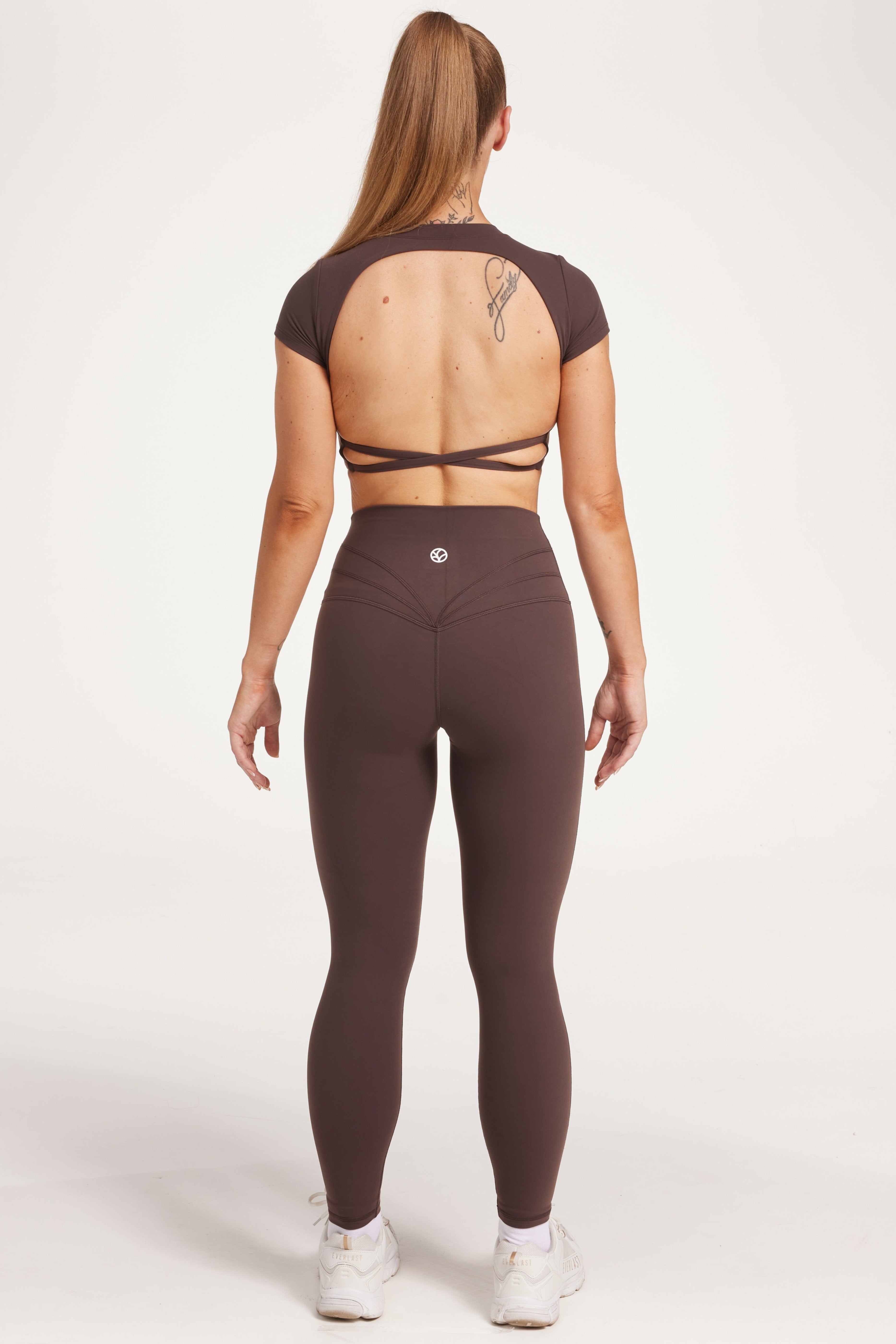 Buttery soft high waisted women's gym tights with curved hem stitched detailing for a butt shaping effect, and no front rise seam, paired with an open back women's crop t-shirt with a supportive elasticated hem and triple layered fabric with removable pads for extra support and aesthetic cross back straps in dark chocolate.