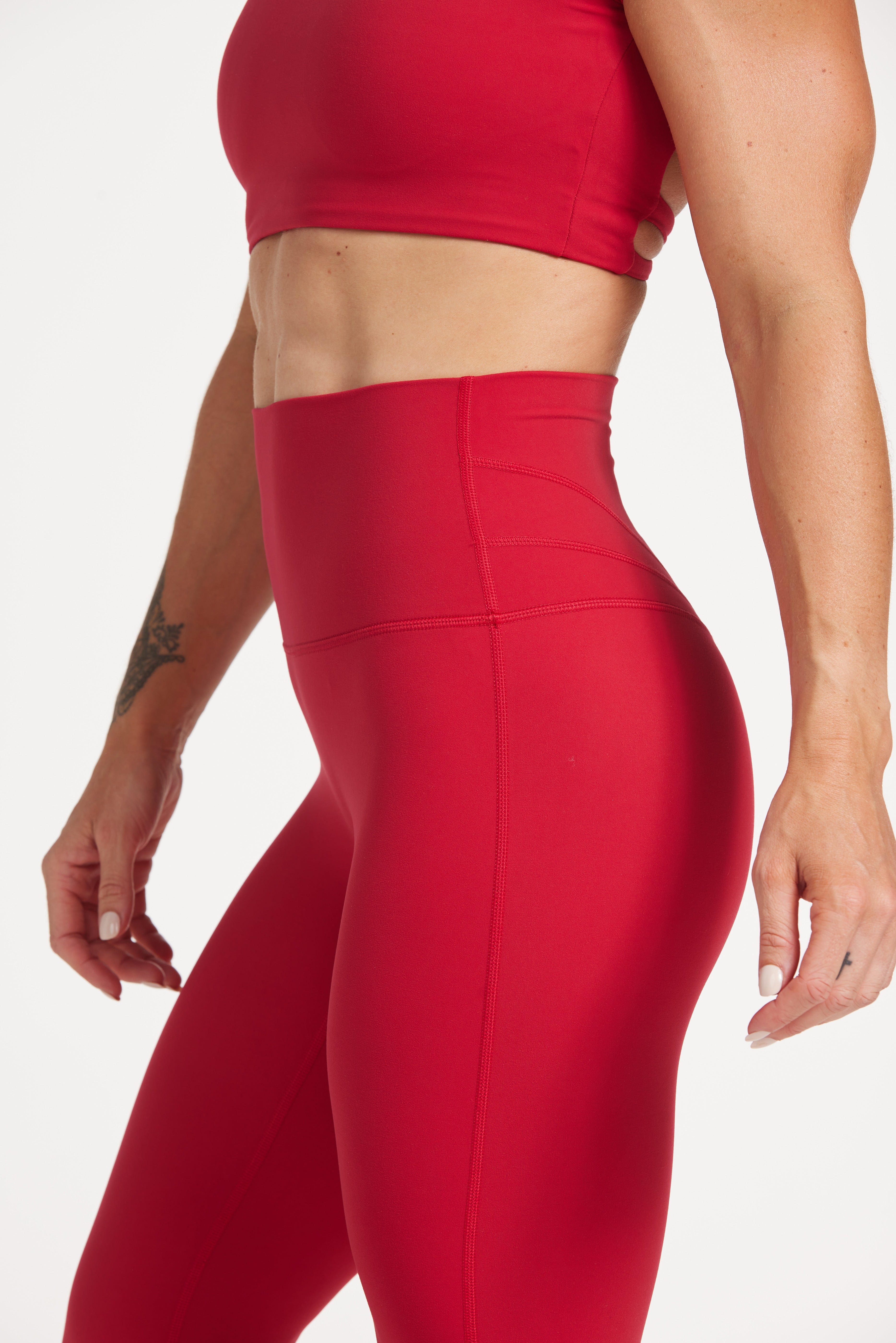 Buttery soft high waisted women's gym tights with curved hem stitched detailing for a butt shaping effect, and no front rise seam, paired with an open back women's crop t-shirt with a supportive elasticated hem and triple layered fabric with removable pads for extra support and aesthetic cross back straps in Raspberry red.