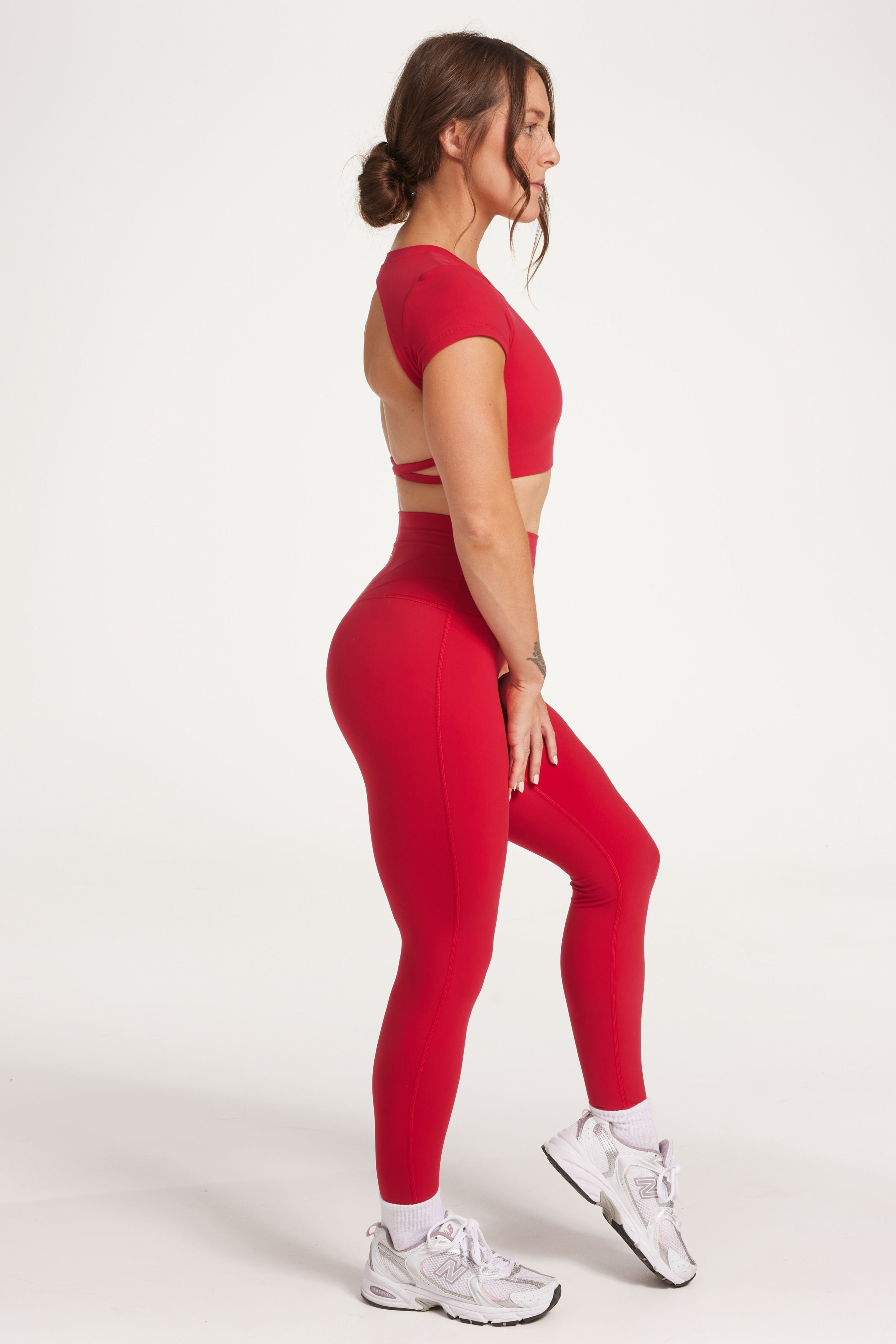 Buttery soft high waisted women's gym tights with curved hem stitched detailing for a butt shaping effect, and no front rise seam, paired with an open back women's crop t-shirt with a supportive elasticated hem and triple layered fabric with removable pads for extra support and aesthetic cross back straps in Raspberry red.