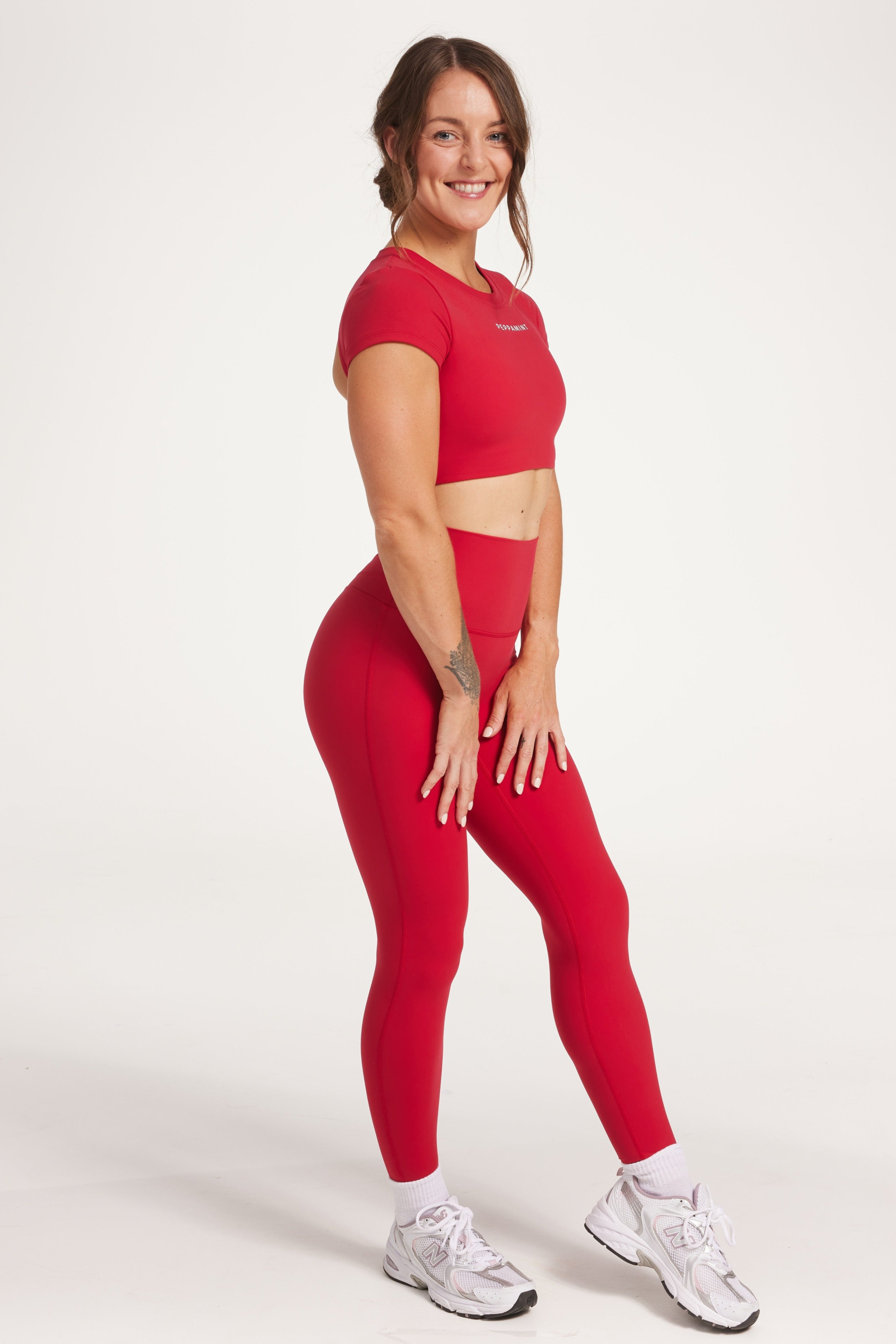 Buttery soft high waisted women's gym tights with curved hem stitched detailing for a butt shaping effect, and no front rise seam, paired with an open back women's crop t-shirt with a supportive elasticated hem and triple layered fabric with removable pads for extra support and aesthetic cross back straps in Raspberry red.
