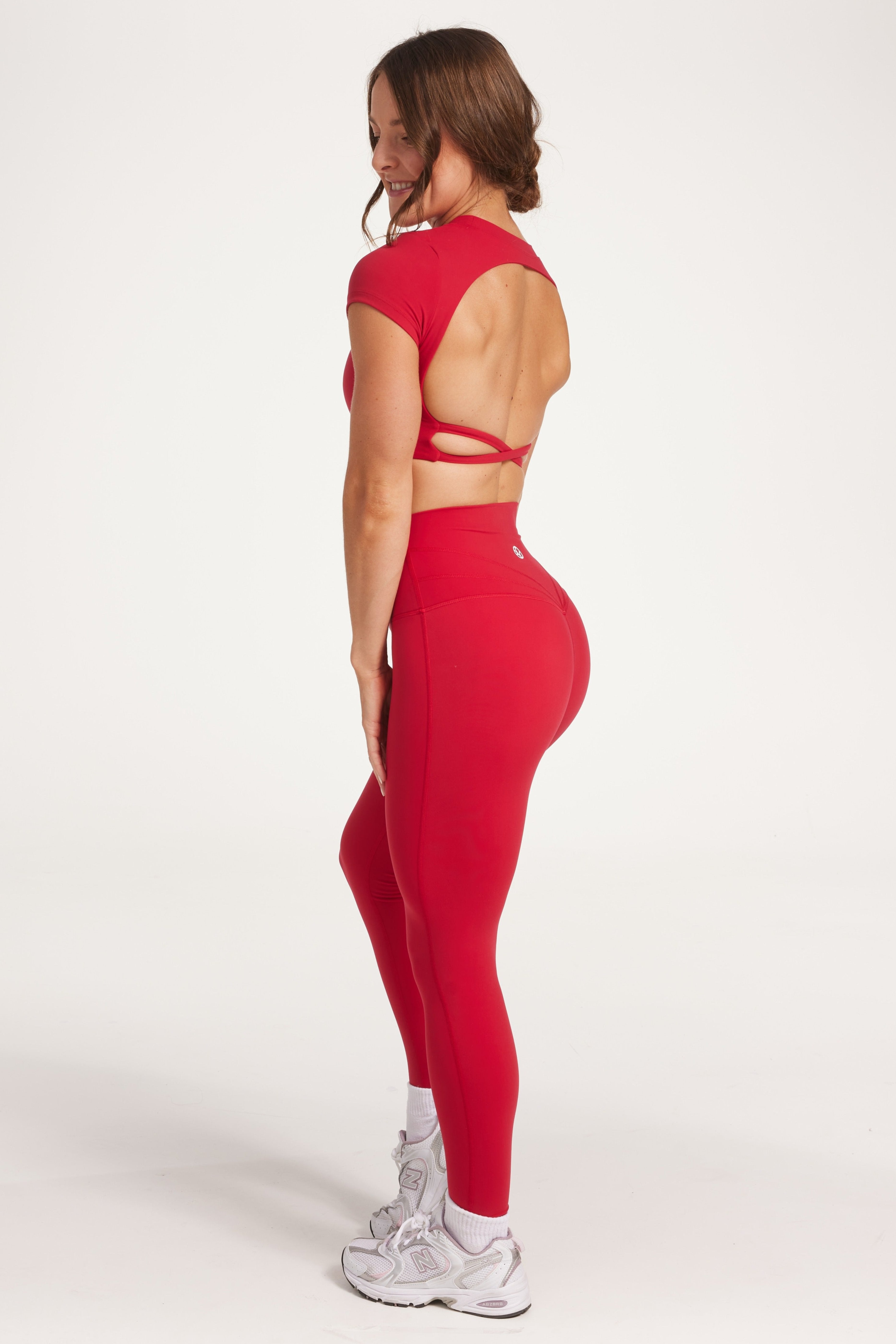 Buttery soft high waisted women's gym tights with curved hem stitched detailing for a butt shaping effect, and no front rise seam, paired with an open back women's crop t-shirt with a supportive elasticated hem and triple layered fabric with removable pads for extra support and aesthetic cross back straps in Raspberry red.