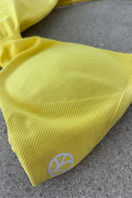 Load image into Gallery viewer, Minimalistic bra with breast contouring panels and a ruched front seam to effortlessy shape the breasts, with a sleek back straps and halter neck design for showcasing the back gains in buttercup yellow