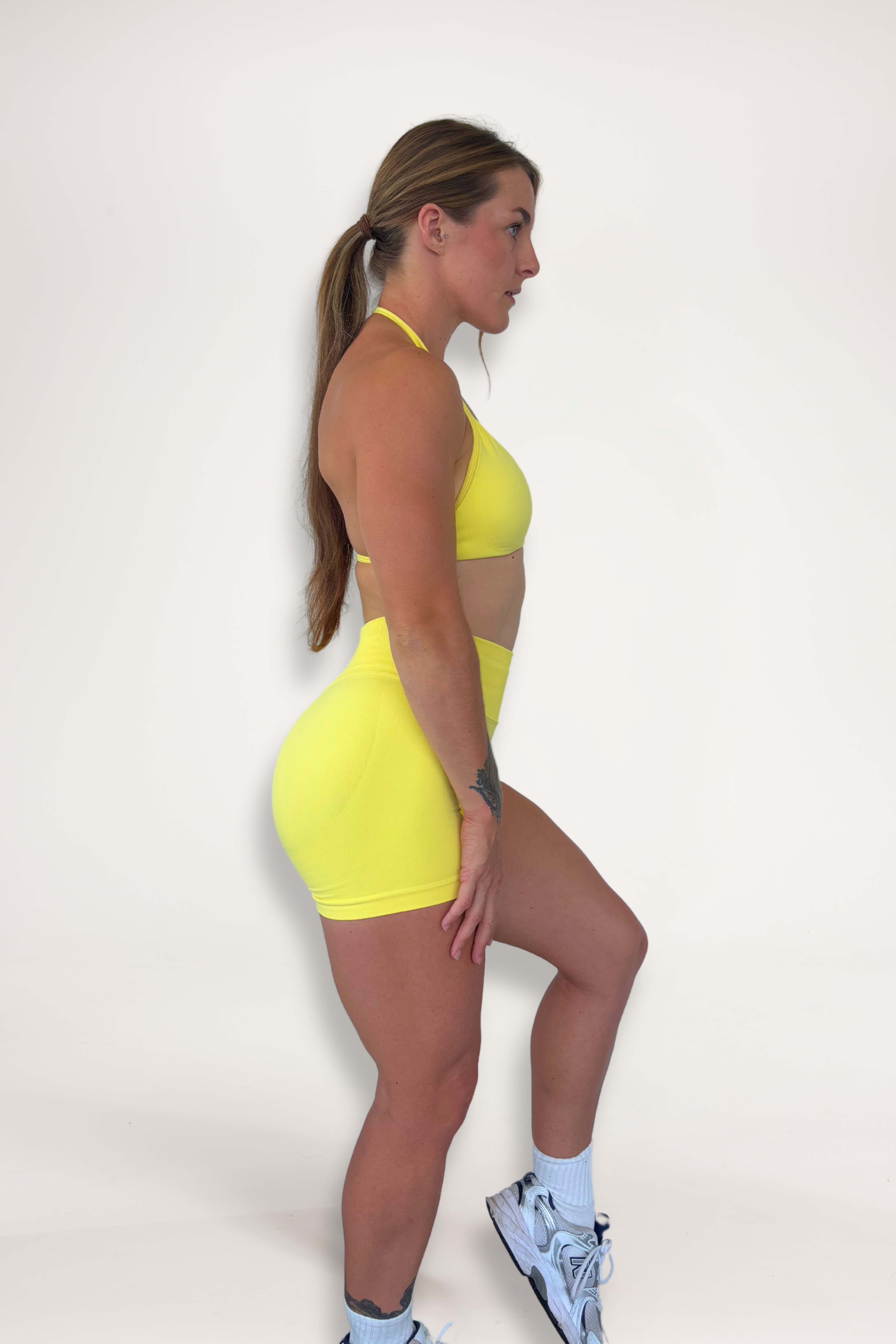 Seamless shorts with booty contouring panels, glute shaping seams, a thick supportive waistband paired with a minimalistic bra with sleek back straps and halter neck design for showcasing the back gains in buttercup yellow