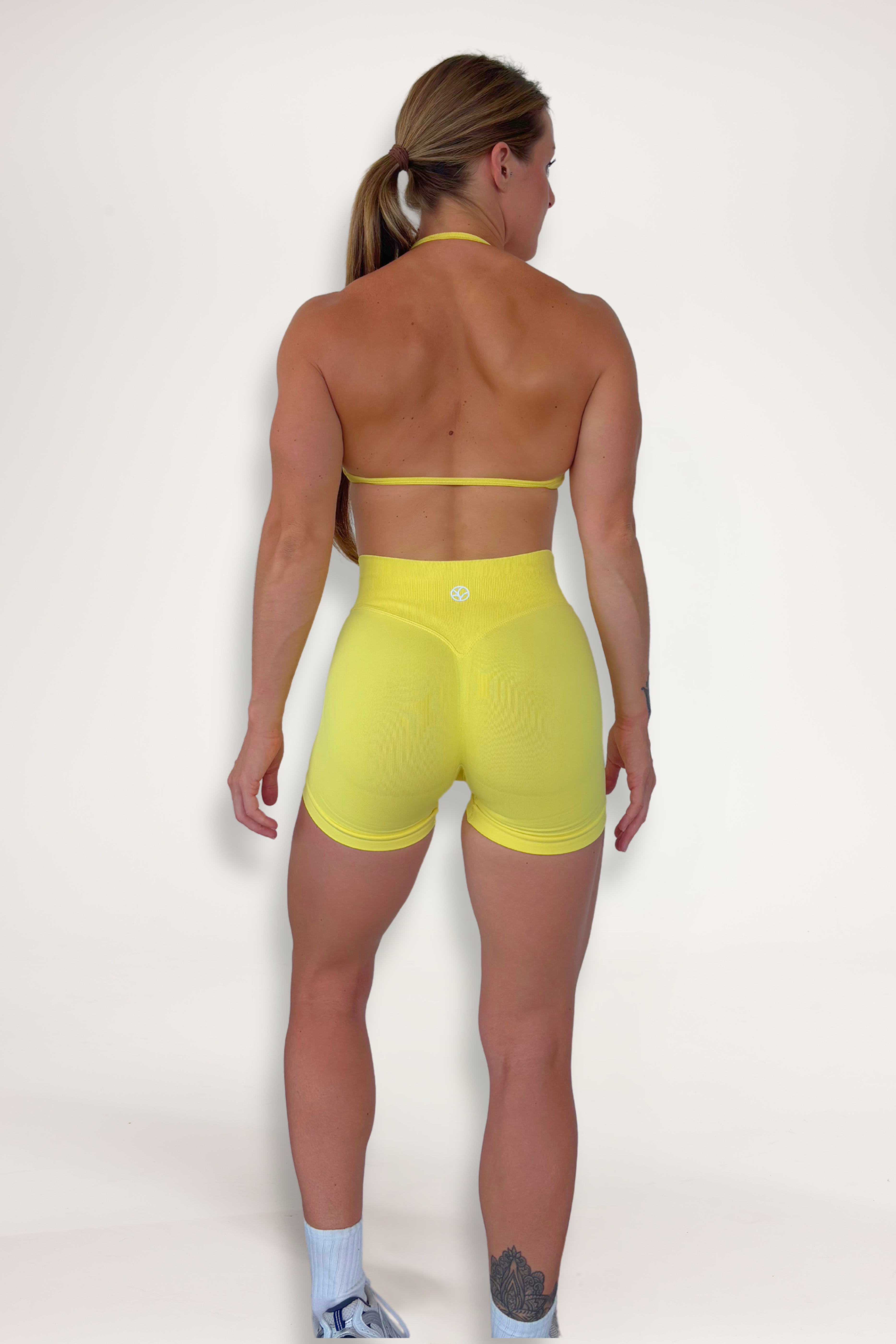 Seamless shorts with booty contouring panels, glute shaping seams, a thick supportive waistband paired with a minimalistic bra with sleek back straps and halter neck design for showcasing the back gains in buttercup yellow