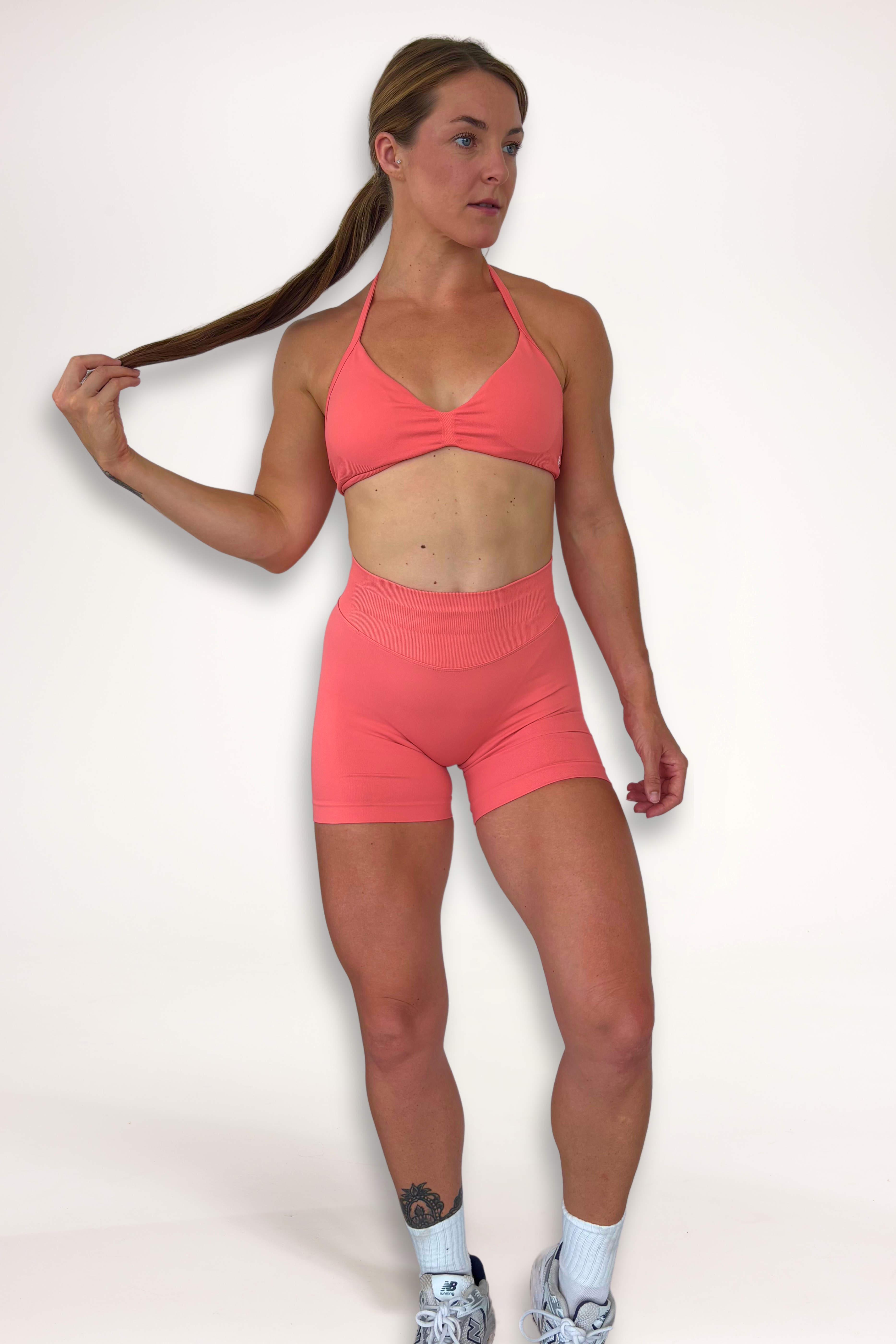 Seamless shorts with booty contouring panels, glute shaping seams, a thick supportive waistband paired with a minimalistic bra with sleek back straps and halter neck design for showcasing the back gains in coral