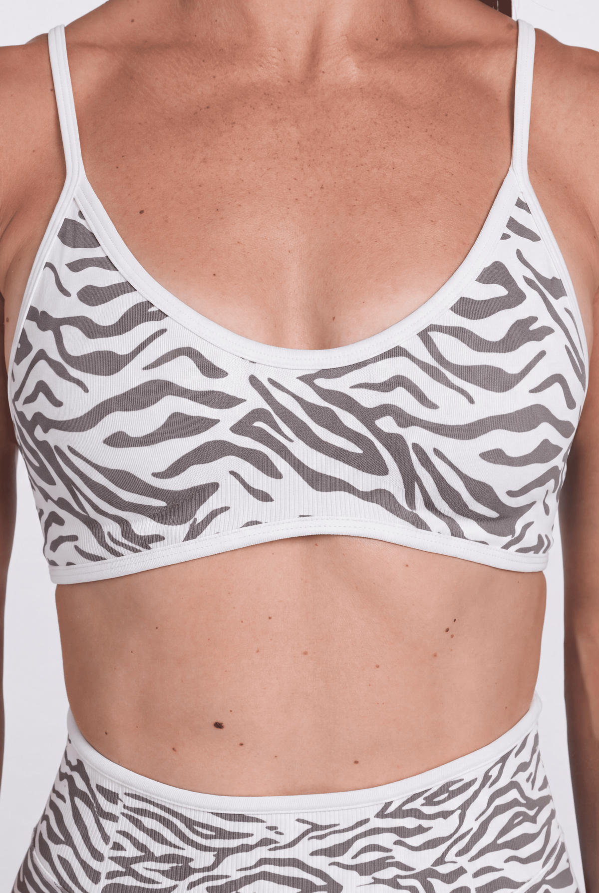 A close-up of a model wearing a white and grey zebra-print sports bra and matching high-waisted shorts against a plain white background.