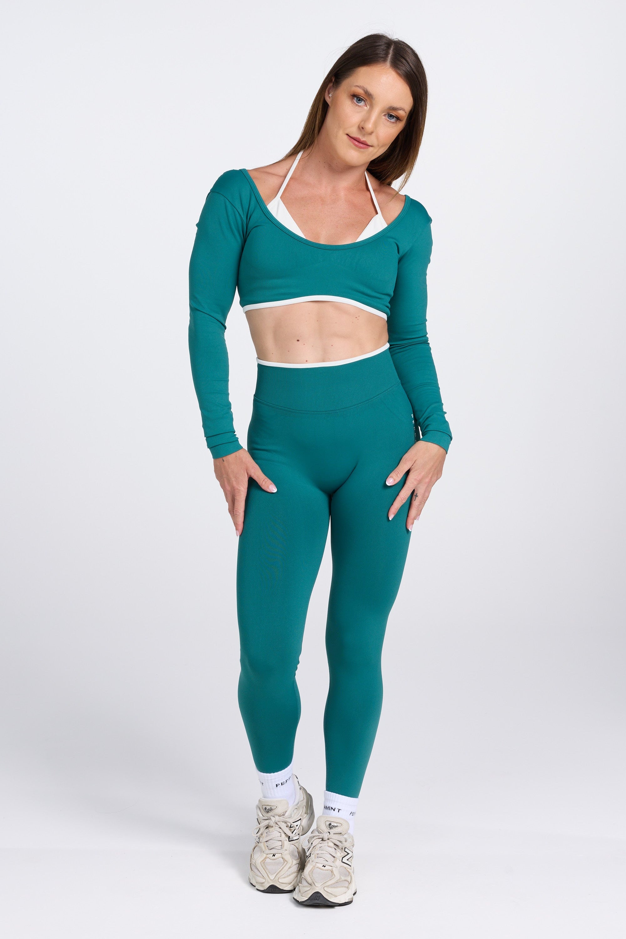 Long sleeve seamless crop top, with built in white contrasting bra, luxe white trim, and adjustable halter strap in teal colour.