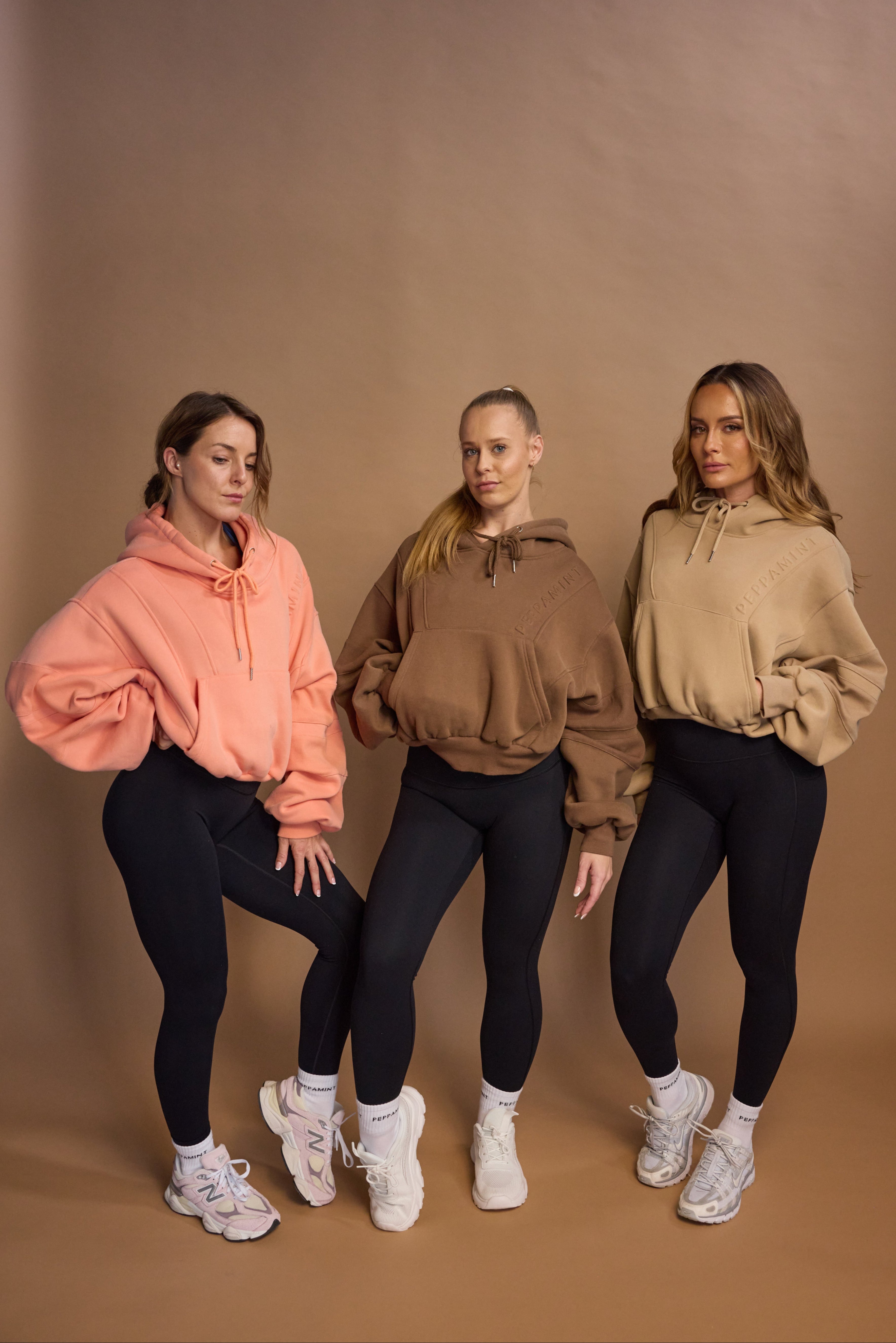 Oversize batwing hoodie, hip length, with slouchy oversized sleeves, piped seams, iconic ribbed panels and a kangaroo pocket with a hidden phone pocket inside in chocolate brown, coral and a beige sand colour