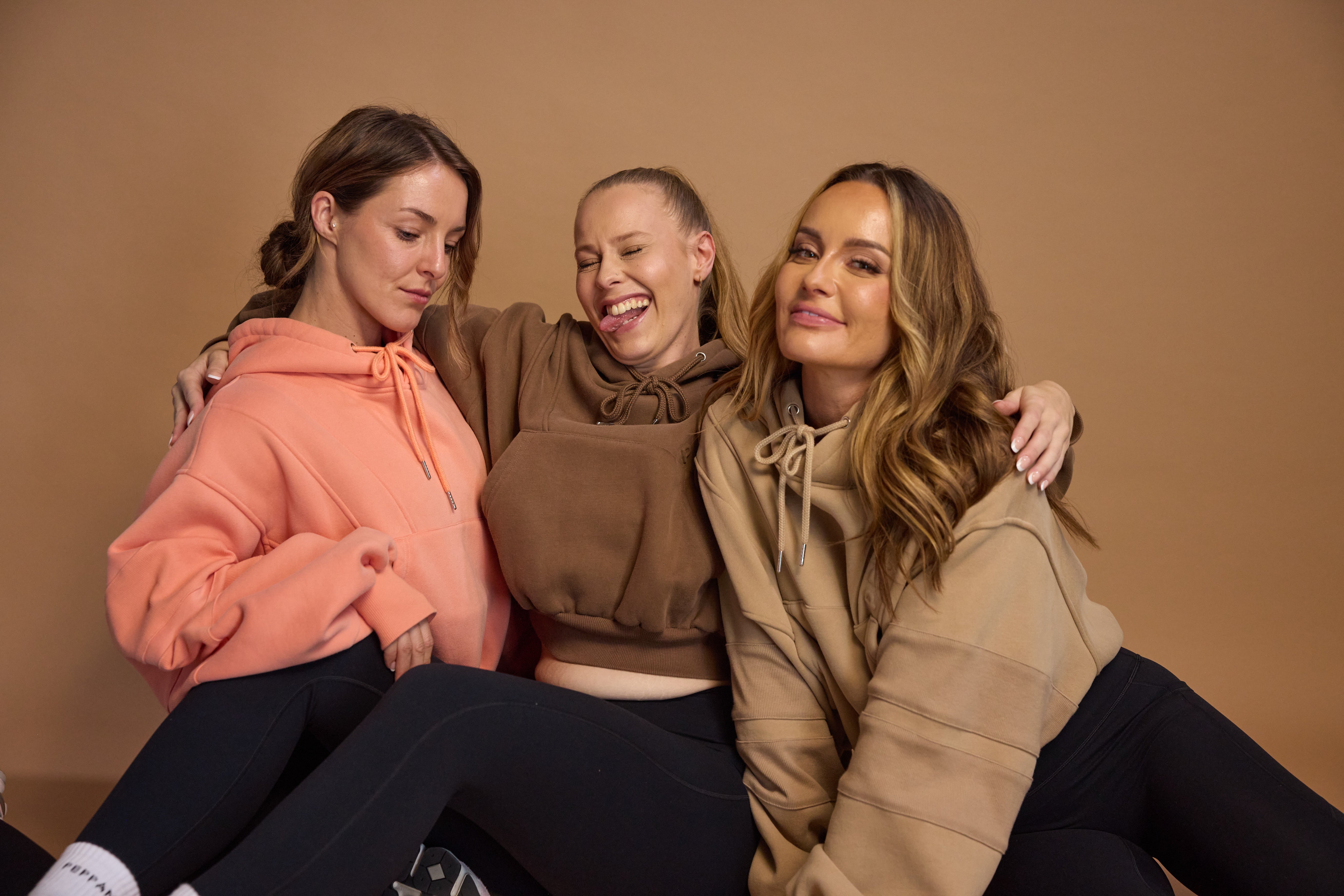Oversize batwing hoodie, hip length, with slouchy oversized sleeves, piped seams, iconic ribbed panels and a kangaroo pocket with a hidden phone pocket inside in chocolate brown, coral and a beige sand colour