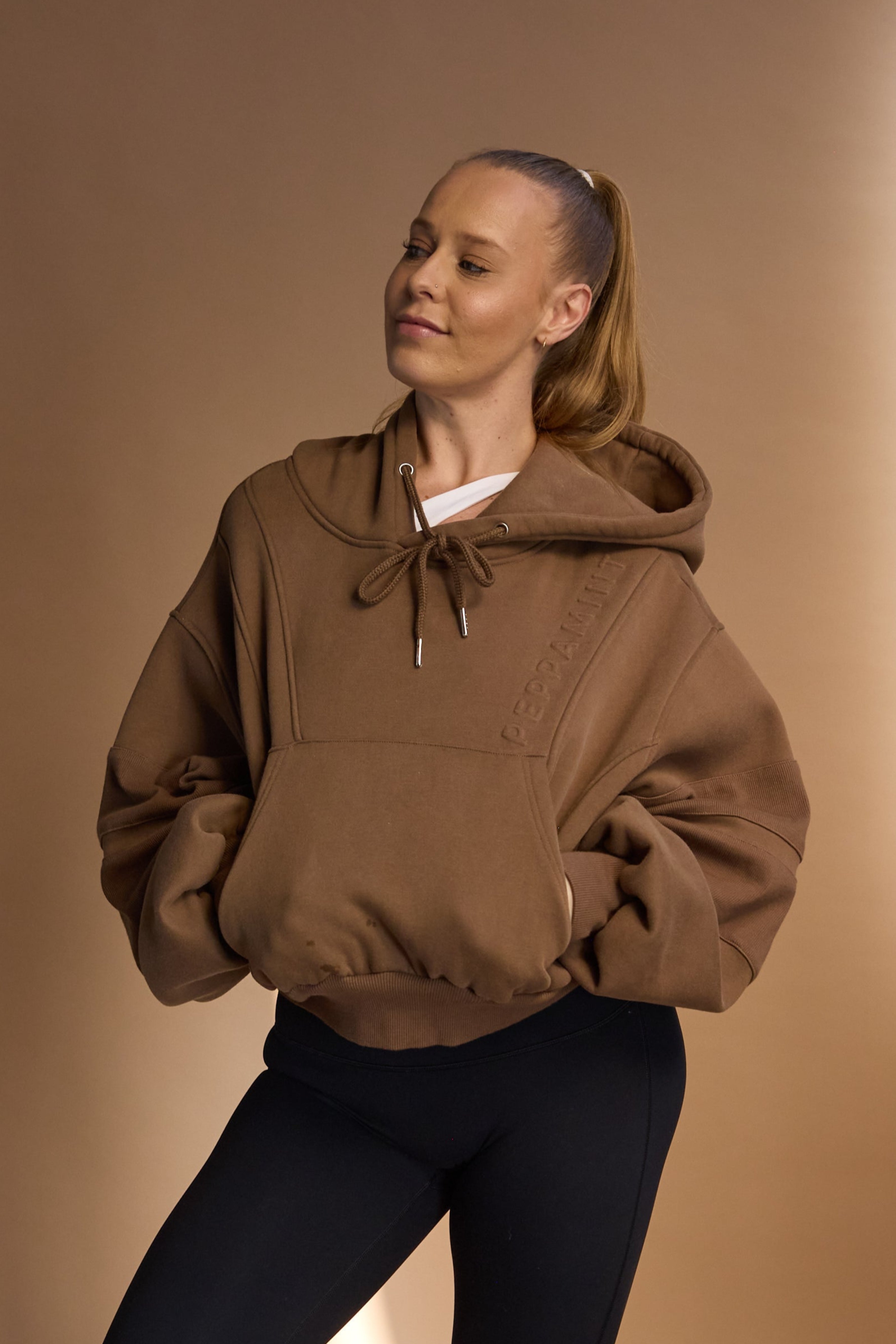 Oversize batwing hoodie, hip length, with slouchy oversized sleeves, piped seams, iconic ribbed panels and a kangaroo pocket with a hidden phone pocket inside in chocolate brown colour