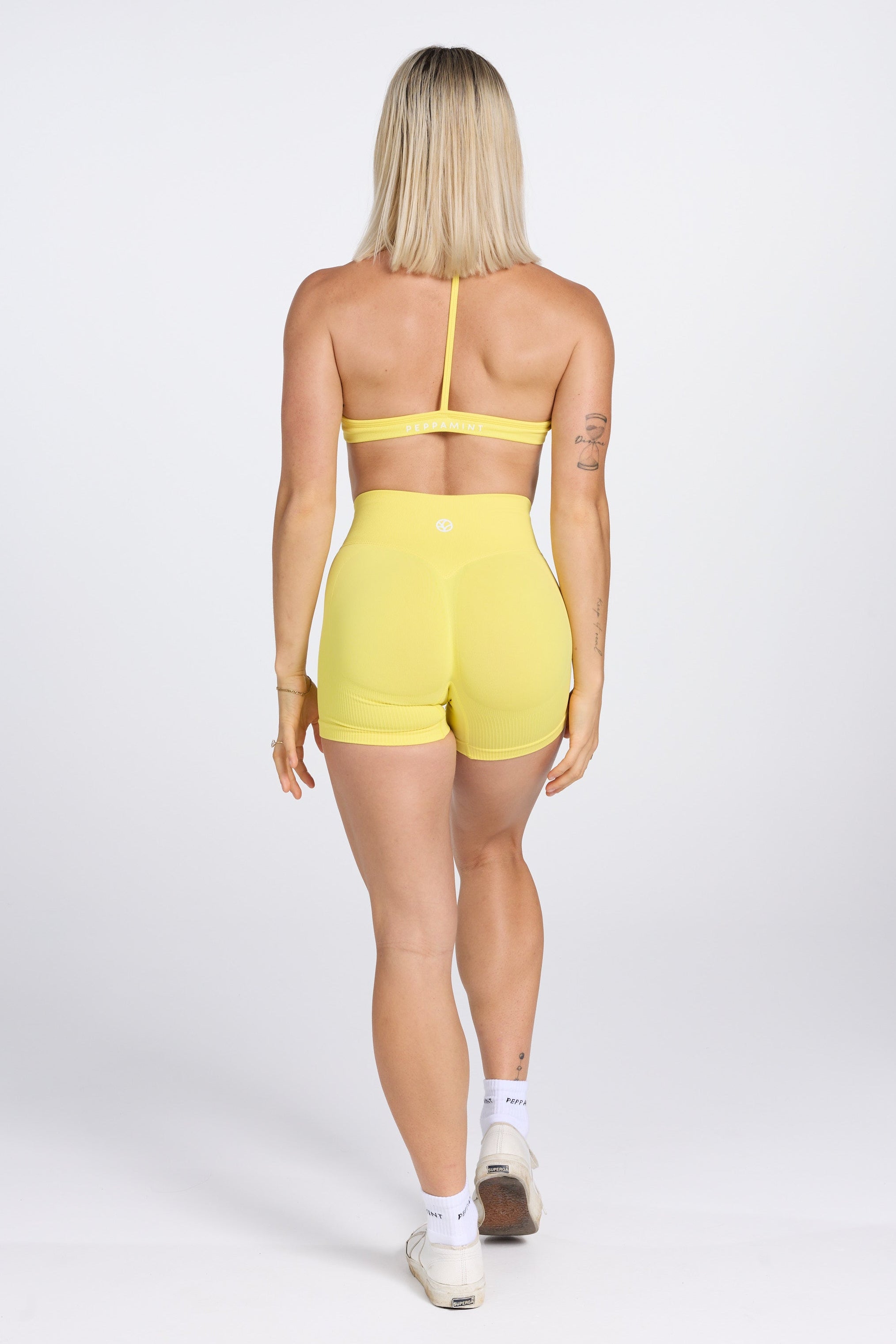 Seamless women’s gym bra with an ultra thin racerback strap design, with white PEPPAMINT branding on the back strap paired with high waisted gym shorts with booty contouring panels, invisible scrunch technology, sweetheart shaped back seams and thick supportive fabric in buttercup yellow