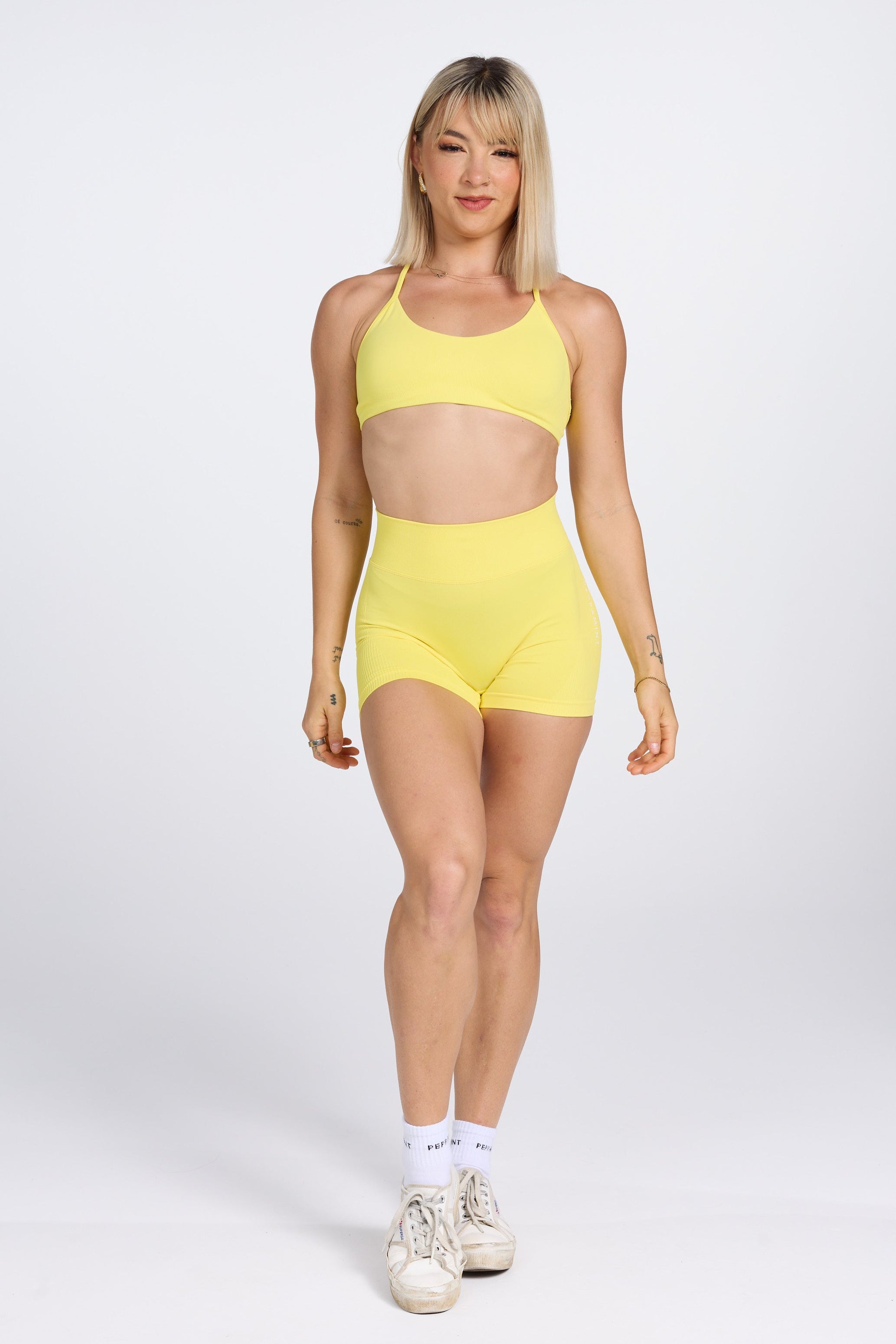 Seamless women’s gym bra with an ultra thin racerback strap design, with white PEPPAMINT branding on the back strap paired with high waisted gym shorts with booty contouring panels, invisible scrunch technology, sweetheart shaped back seams and thick supportive fabric in buttercup yellow