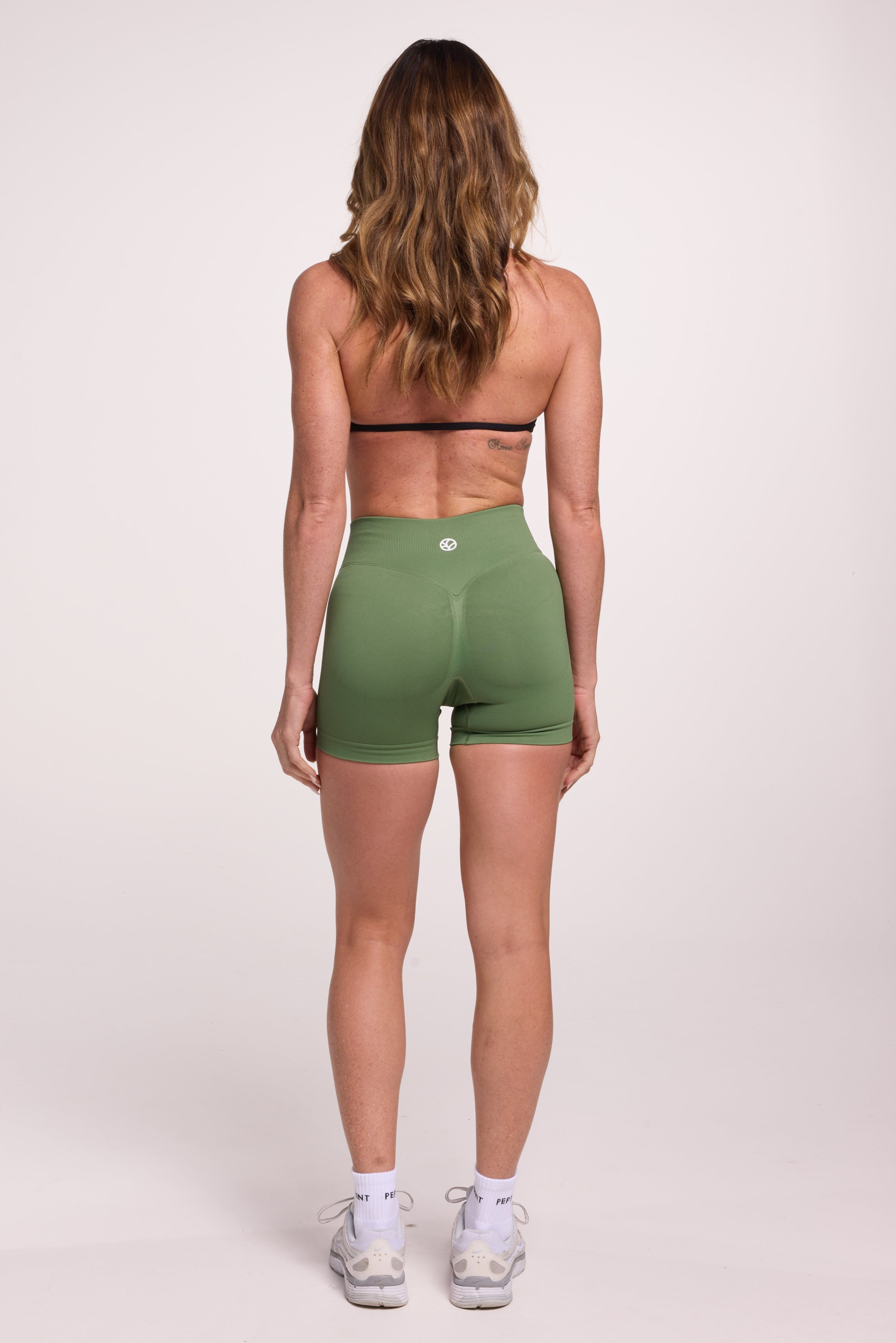 Minimalistic bra with breast contouring panels and a ruched front seam to effortlessly shape the breasts, with a sleek back straps and halter neck design in black and seamless gym tights with booty contouring panels, invisible scrunch technology, sweetheart shaped back seams and thick supportive fabric in mermaid green colour