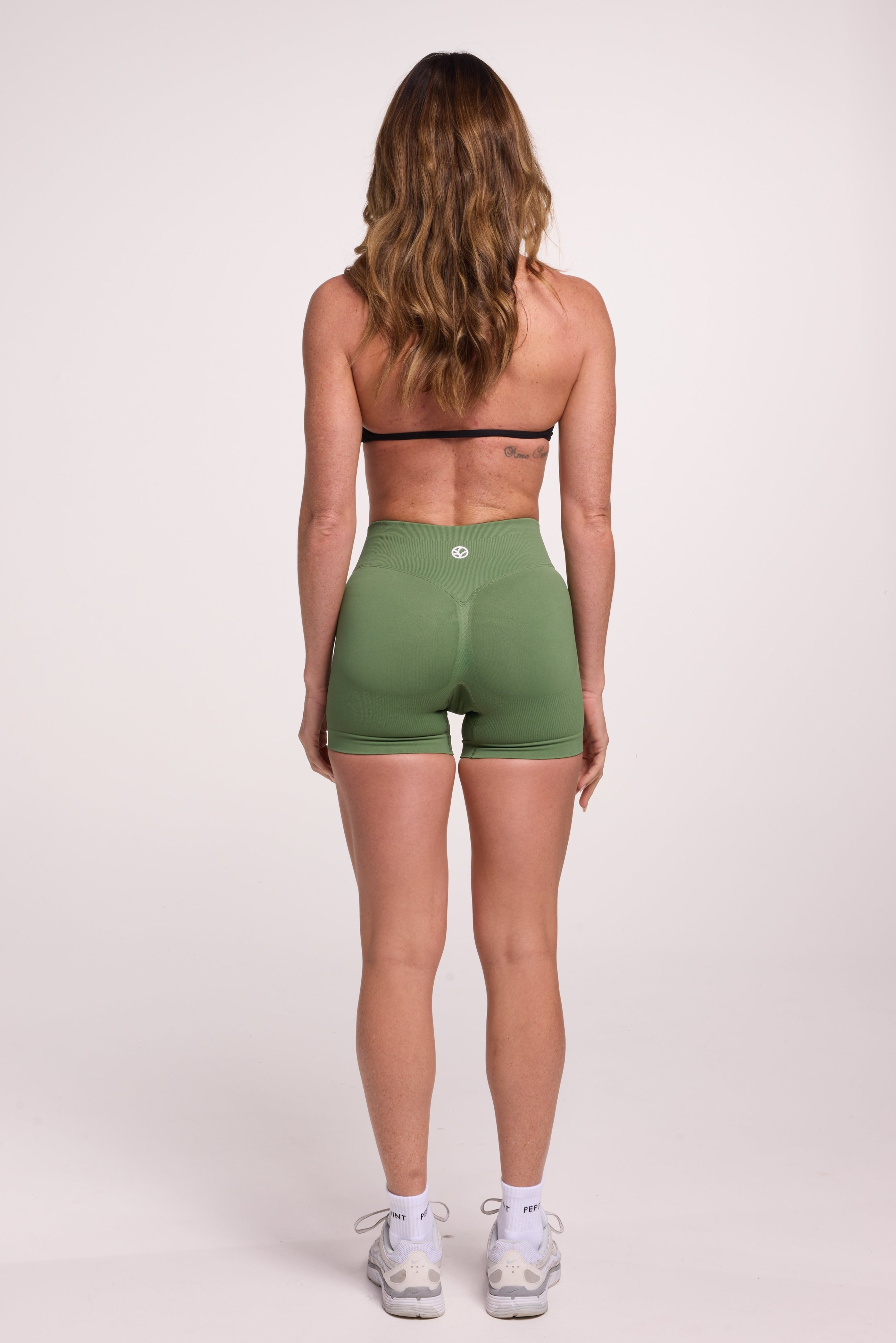 Minimalistic bra with breast contouring panels and a ruched front seam to effortlessly shape the breasts, with a sleek back straps and halter neck design in black and seamless gym tights with booty contouring panels, invisible scrunch technology, sweetheart shaped back seams and thick supportive fabric in mermaid green colour