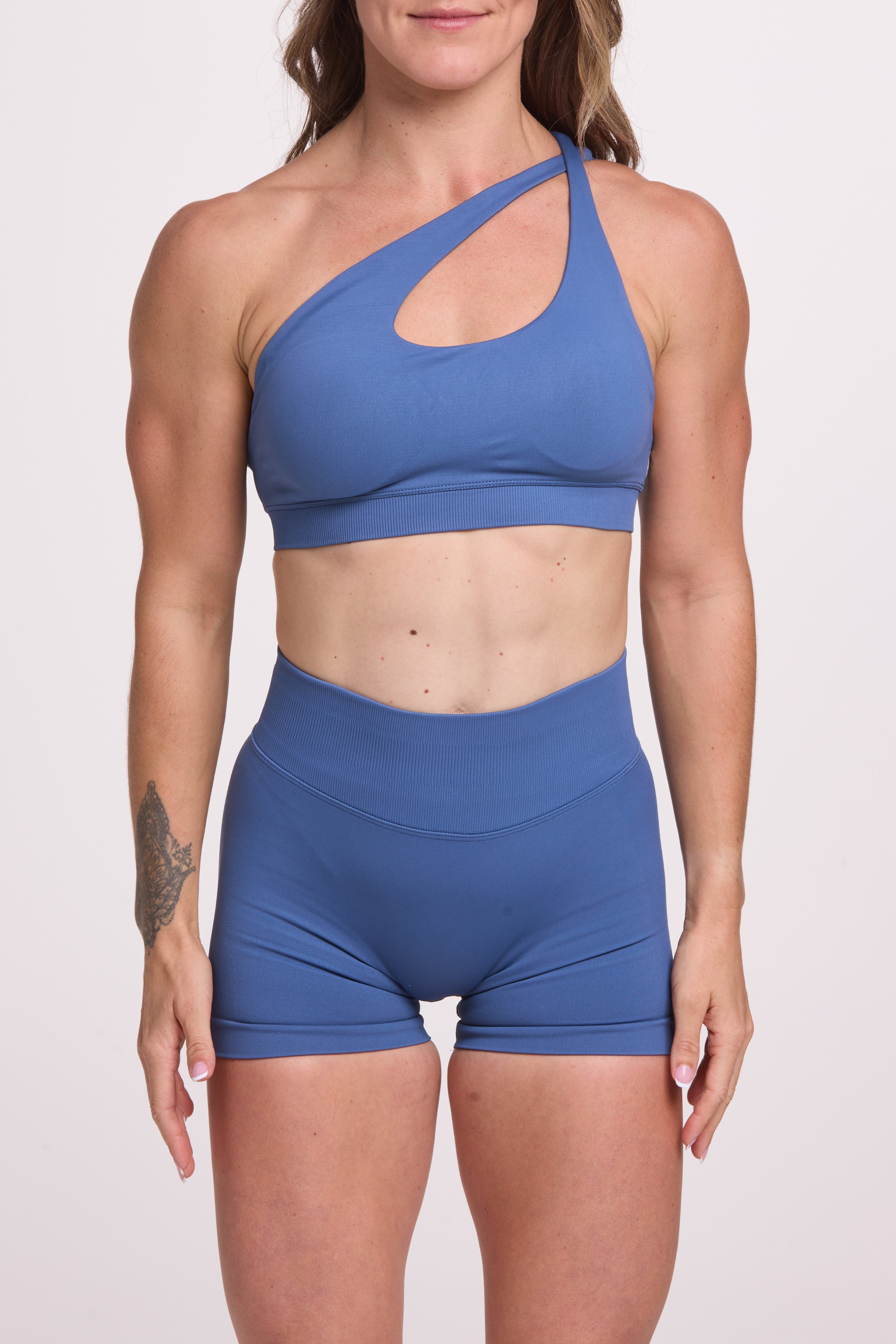 Front cross over strap activewear bra in seamless fabric with adjustable back straps, and ribbed supportive underbust band and seamless gym tights with booty contouring panels, invisible scrunch technology, sweetheart shaped back seams and thick supportive fabric in grey blue colour