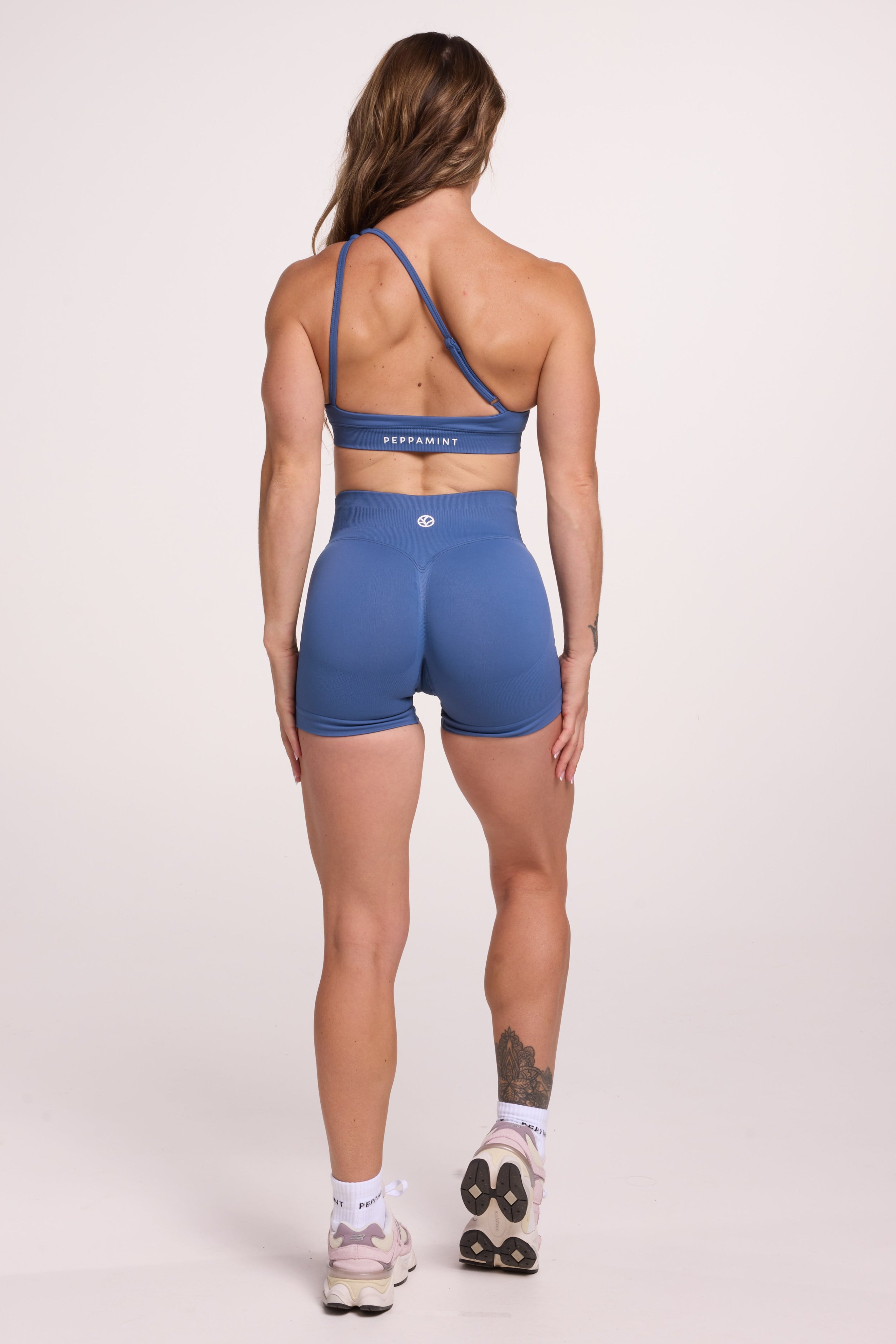Front cross over strap activewear bra in seamless fabric with adjustable back straps, and ribbed supportive underbust band and seamless gym tights with booty contouring panels, invisible scrunch technology, sweetheart shaped back seams and thick supportive fabric in grey blue colour
