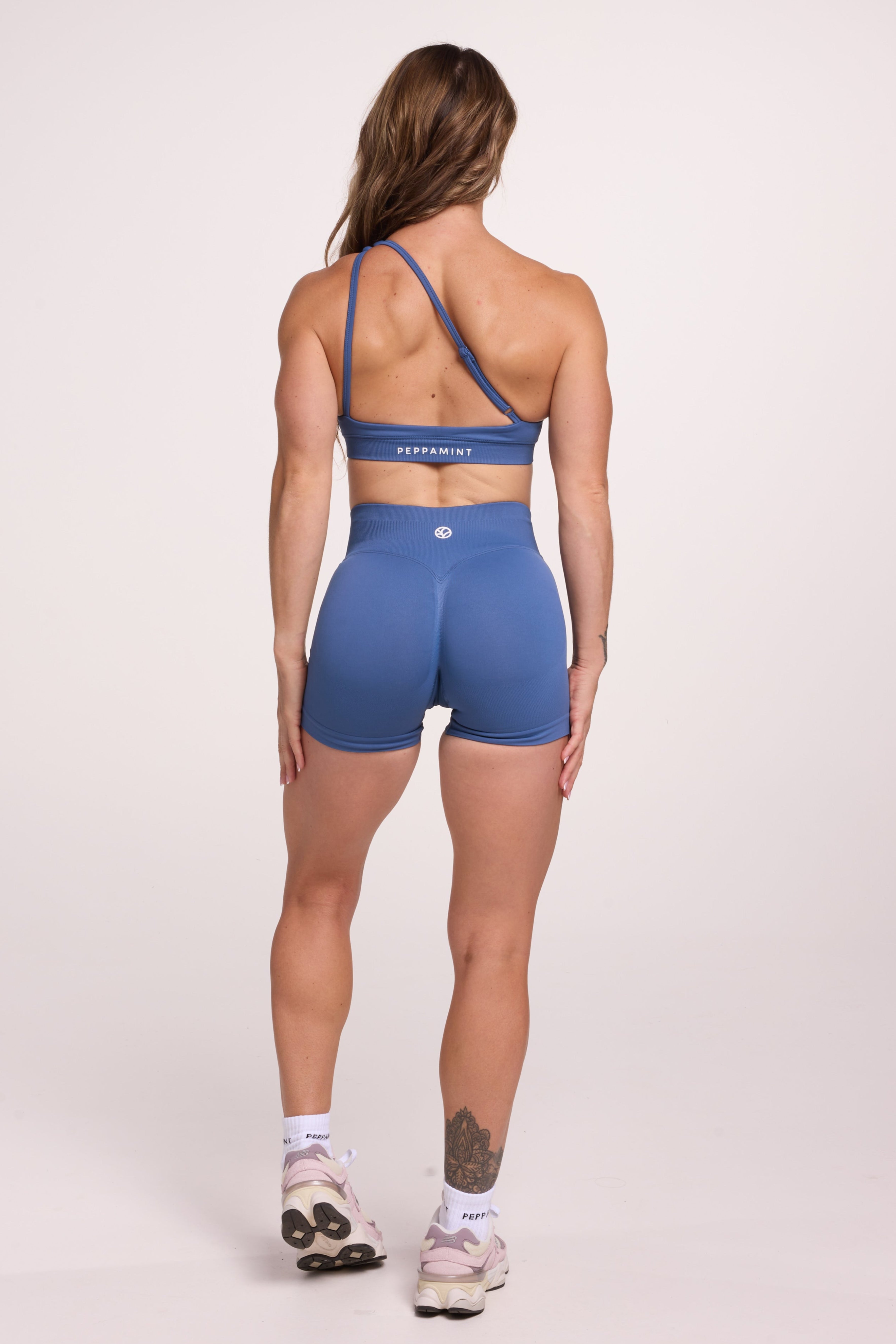Front cross over strap activewear bra in seamless fabric with adjustable back straps, and ribbed supportive underbust band and seamless gym tights with booty contouring panels, invisible scrunch technology, sweetheart shaped back seams and thick supportive fabric in grey blue colour