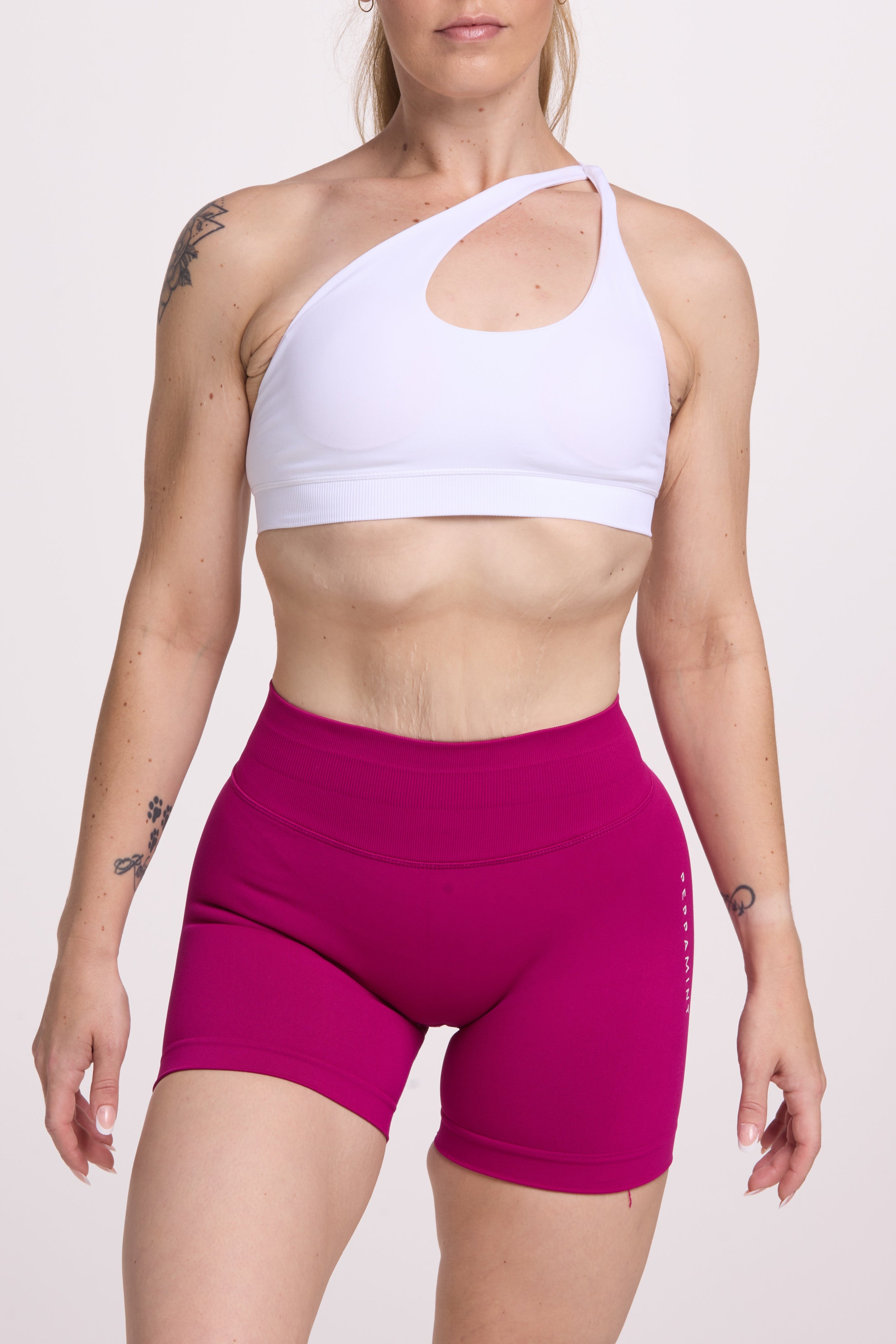 Front cross over strap activewear bra in seamless fabric with adjustable back straps, and ribbed supportive underbust band in white and seamless gym tights with booty contouring panels, invisible scrunch technology, sweetheart shaped back seams and thick supportive fabric in magenta pink