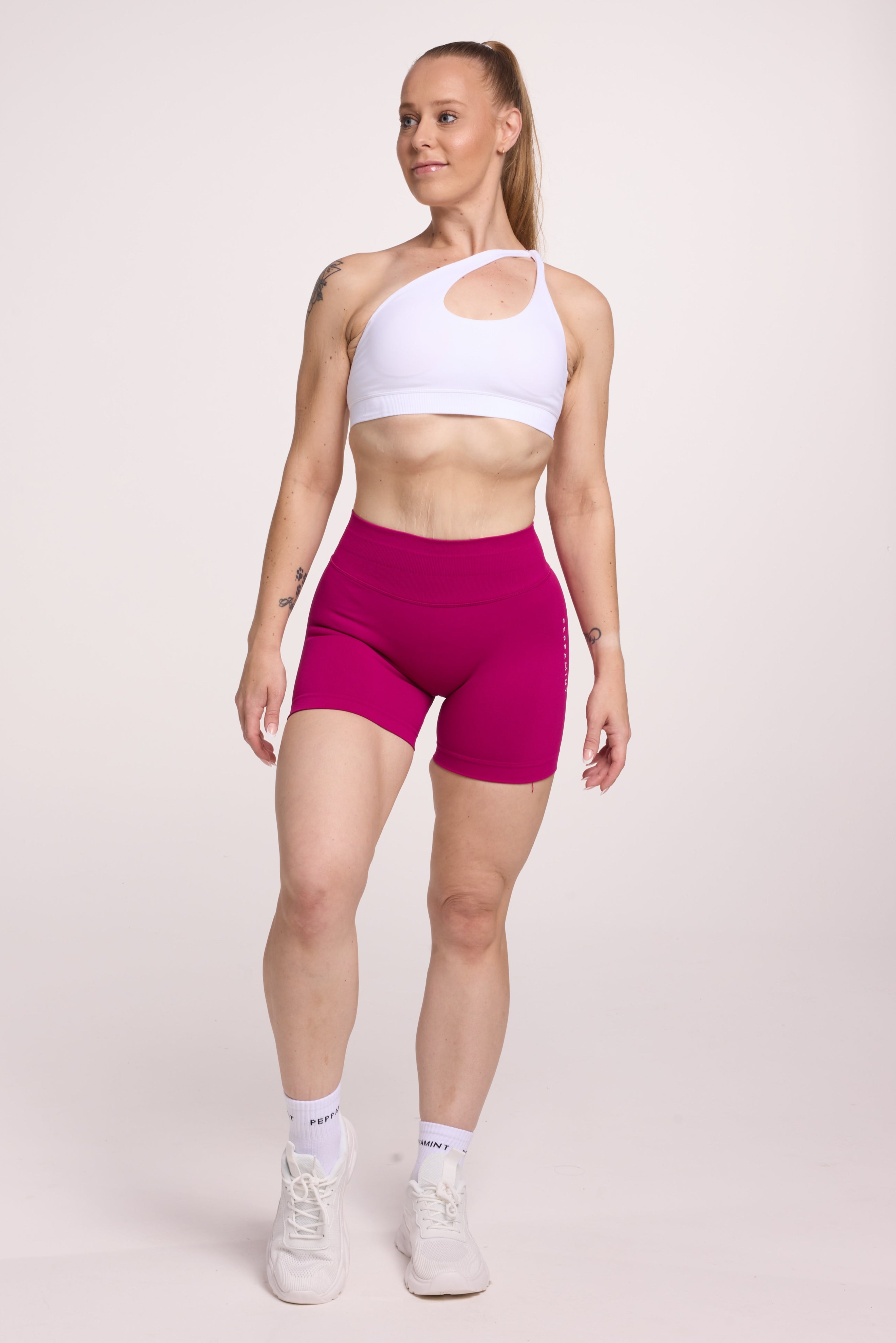Front cross over strap activewear bra in seamless fabric with adjustable back straps, and ribbed supportive underbust band in white and seamless gym tights with booty contouring panels, invisible scrunch technology, sweetheart shaped back seams and thick supportive fabric in magenta pink