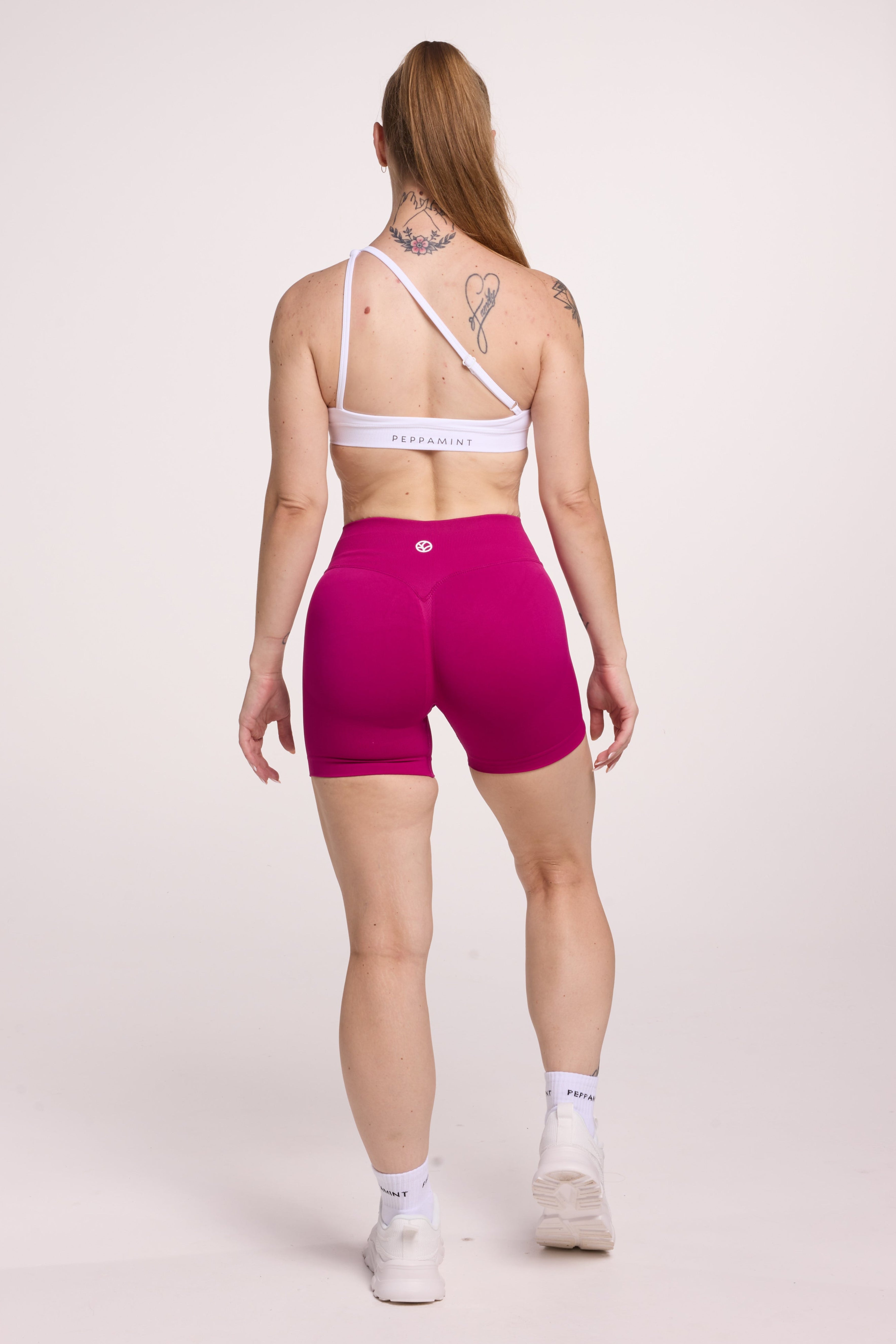 Front cross over strap activewear bra in seamless fabric with adjustable back straps, and ribbed supportive underbust band in white and seamless gym tights with booty contouring panels, invisible scrunch technology, sweetheart shaped back seams and thick supportive fabric in magenta pink
