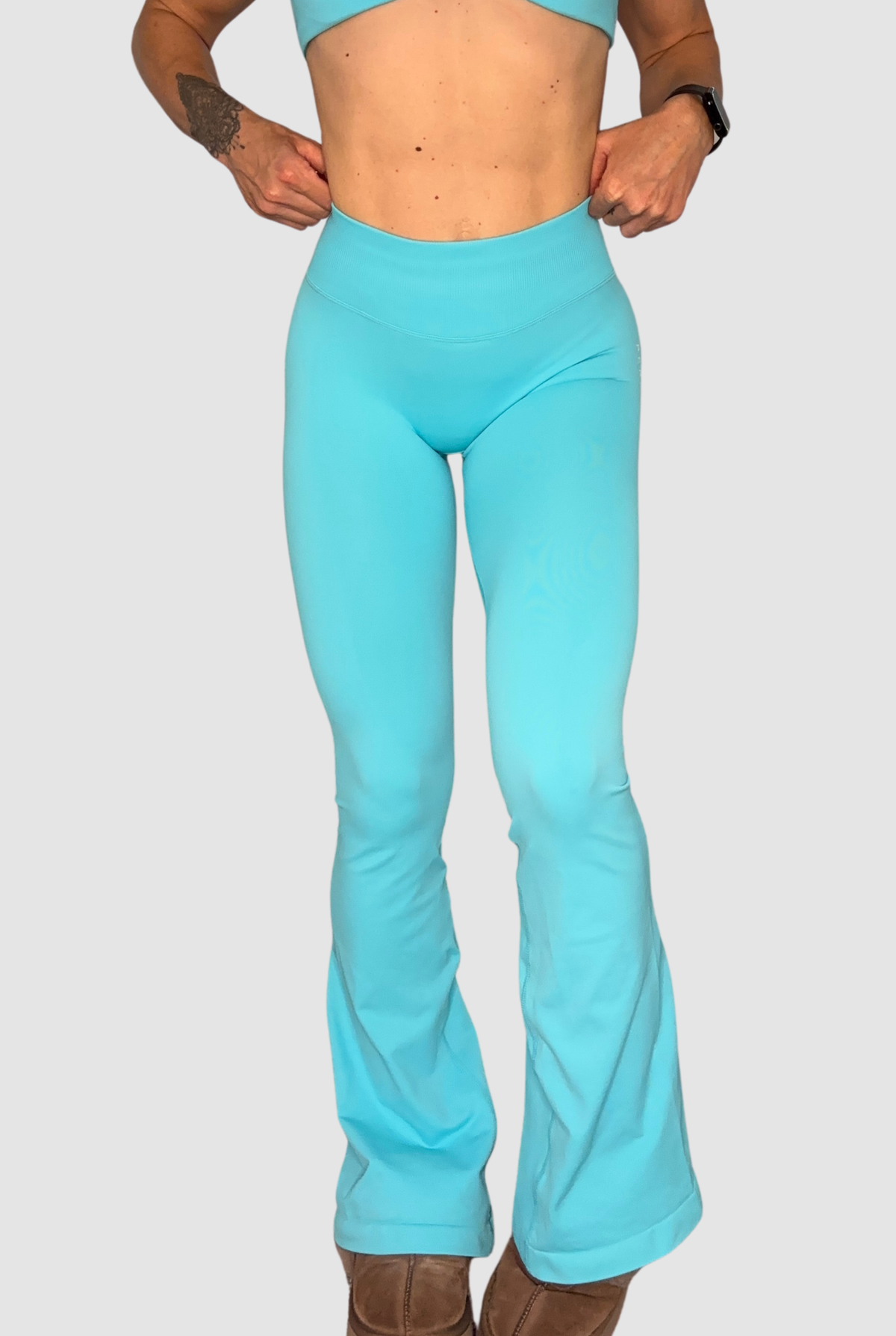 A model wearing bright turquoise high-waisted flared leggings, shown from the waist down against a solid light grey background.