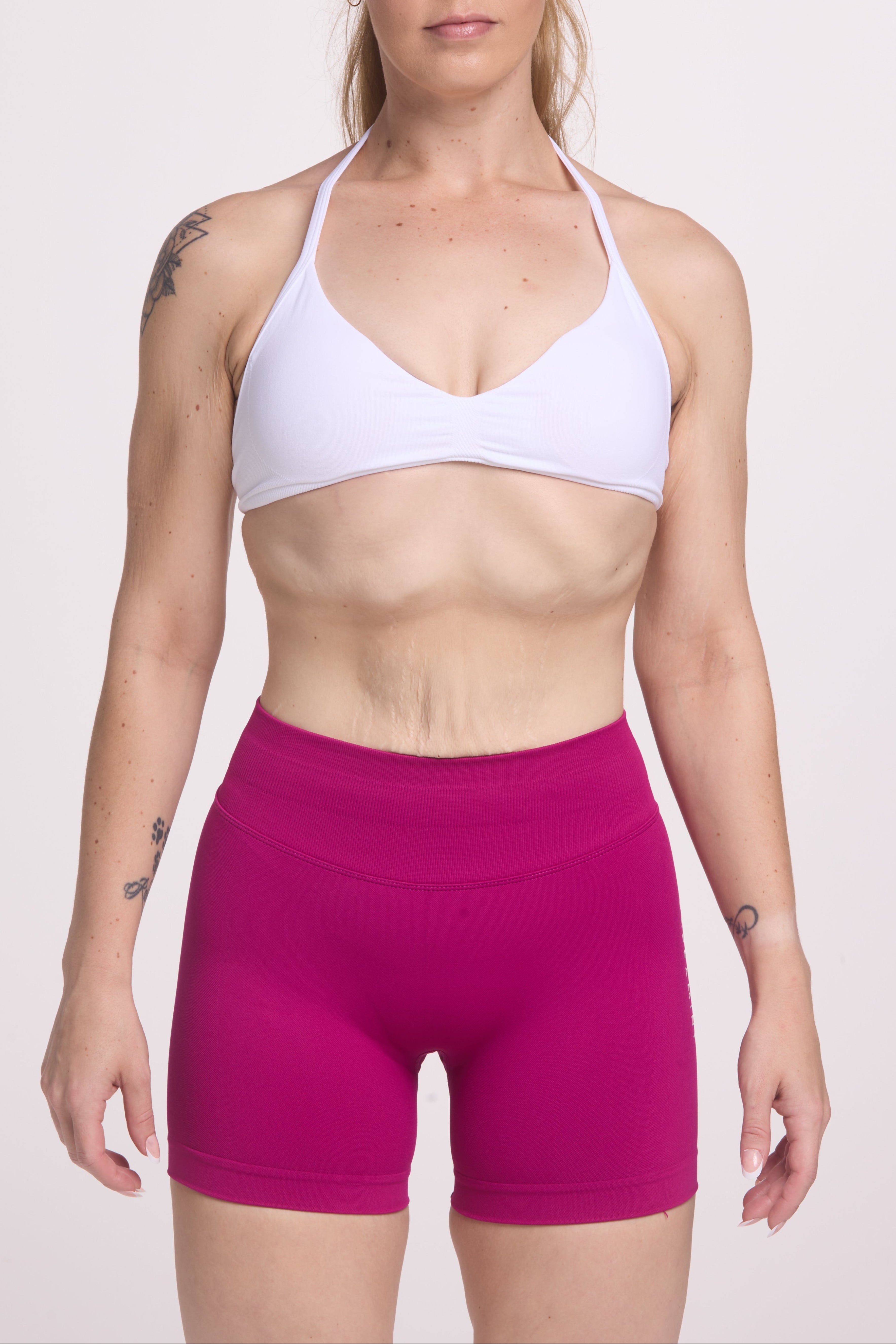 Minimalistic bra with breast contouring panels and a ruched front seam to effortlessly shape the breasts, with a sleek back straps and halter neck design in white and seamless gym tights with booty contouring panels, invisible scrunch technology, sweetheart shaped back seams and thick supportive fabric in magenta colour