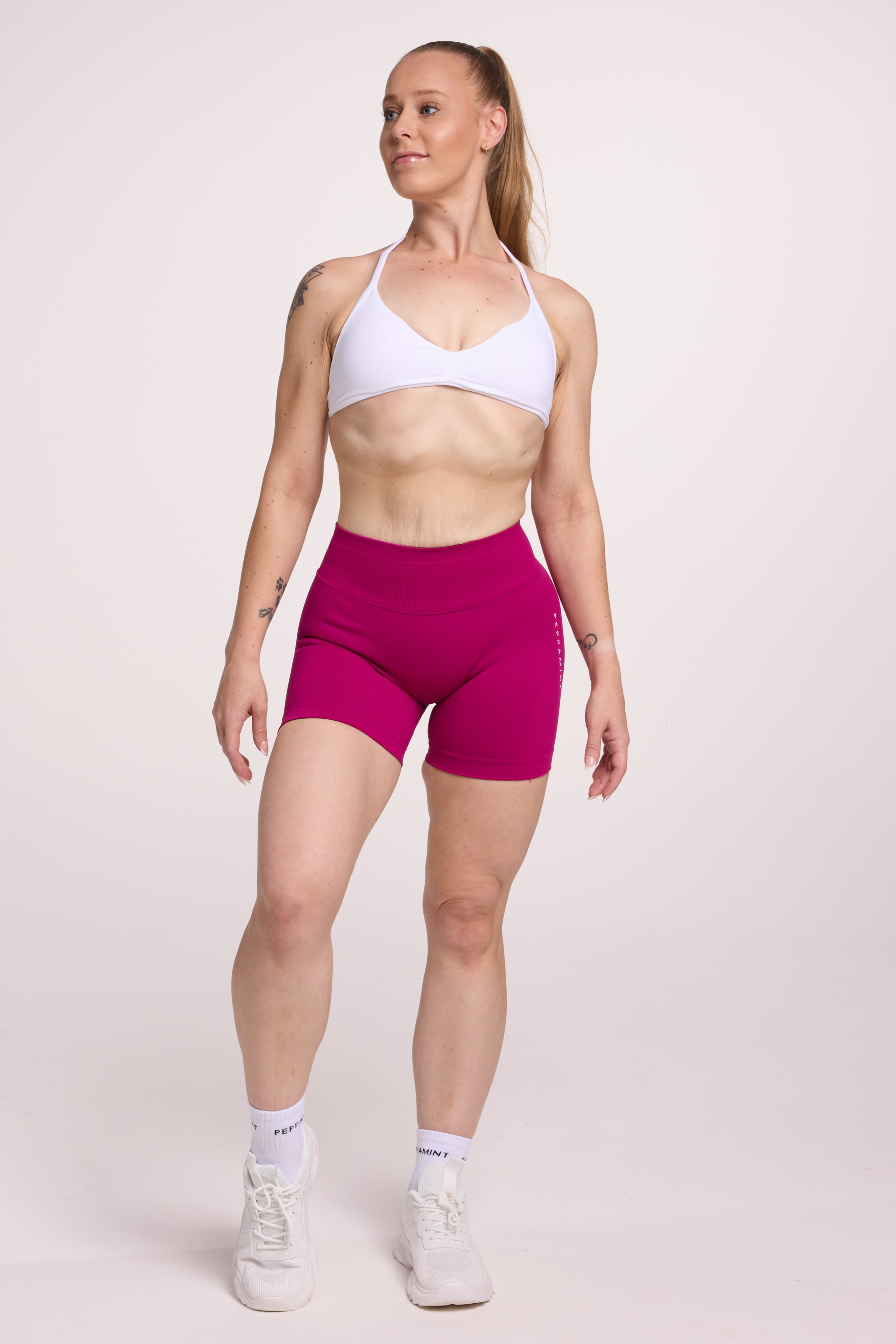 Minimalistic bra with breast contouring panels and a ruched front seam to effortlessly shape the breasts, with a sleek back straps and halter neck design in white and seamless gym tights with booty contouring panels, invisible scrunch technology, sweetheart shaped back seams and thick supportive fabric in magenta colour