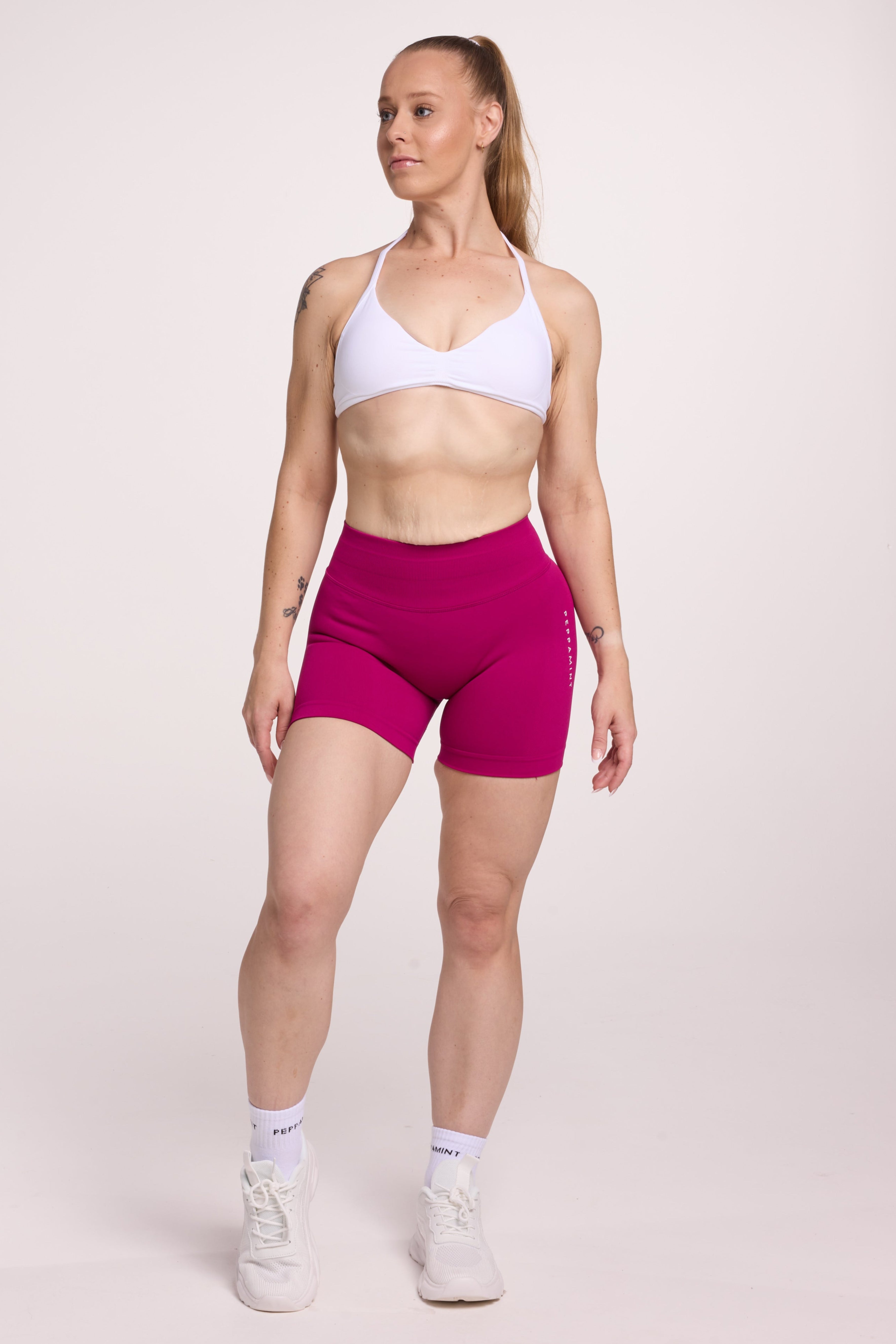 Minimalistic bra with breast contouring panels and a ruched front seam to effortlessly shape the breasts, with a sleek back straps and halter neck design in white and seamless gym tights with booty contouring panels, invisible scrunch technology, sweetheart shaped back seams and thick supportive fabric in magenta colour