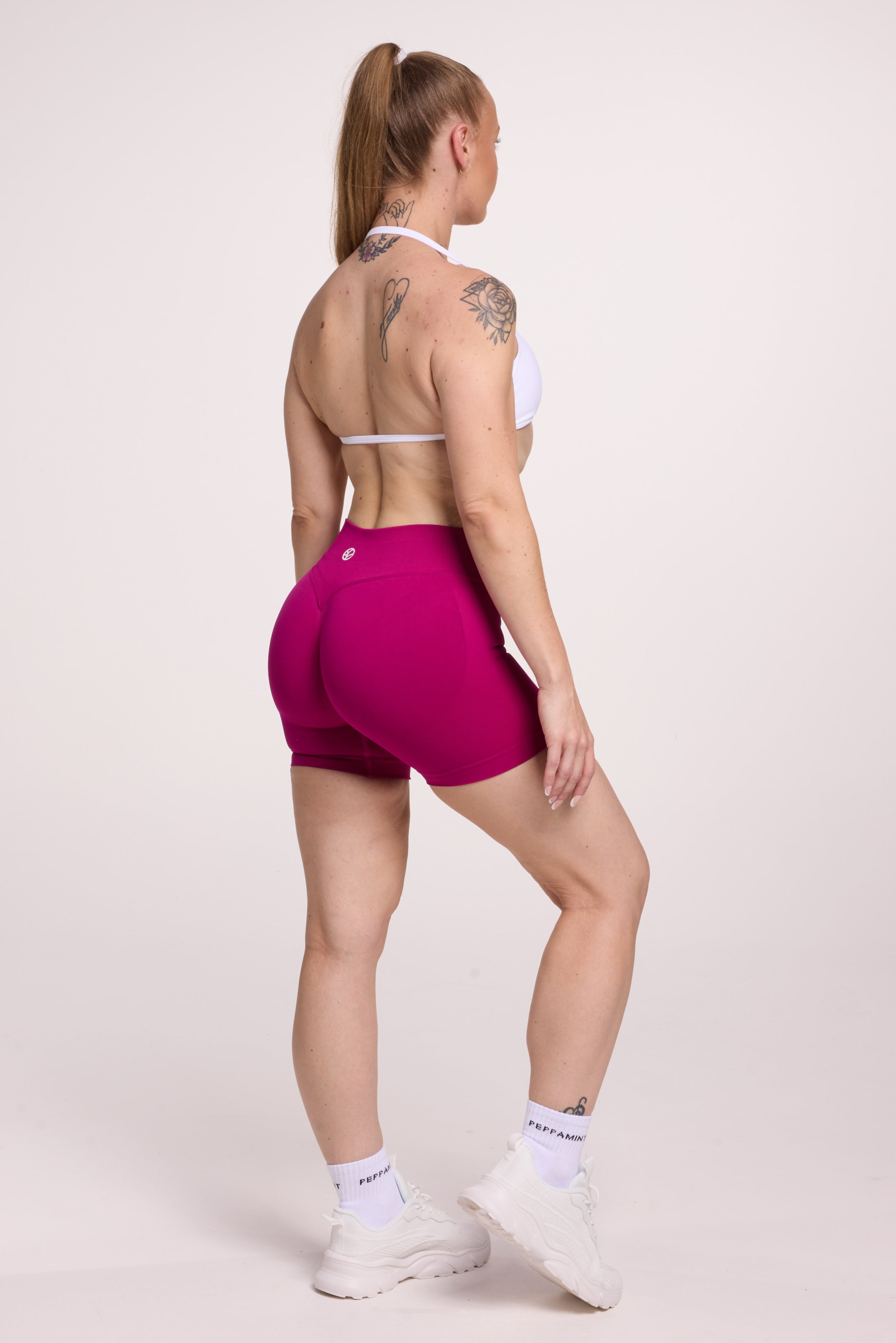 Minimalistic bra with breast contouring panels and a ruched front seam to effortlessly shape the breasts, with a sleek back straps and halter neck design in white and seamless gym tights with booty contouring panels, invisible scrunch technology, sweetheart shaped back seams and thick supportive fabric in magenta colour