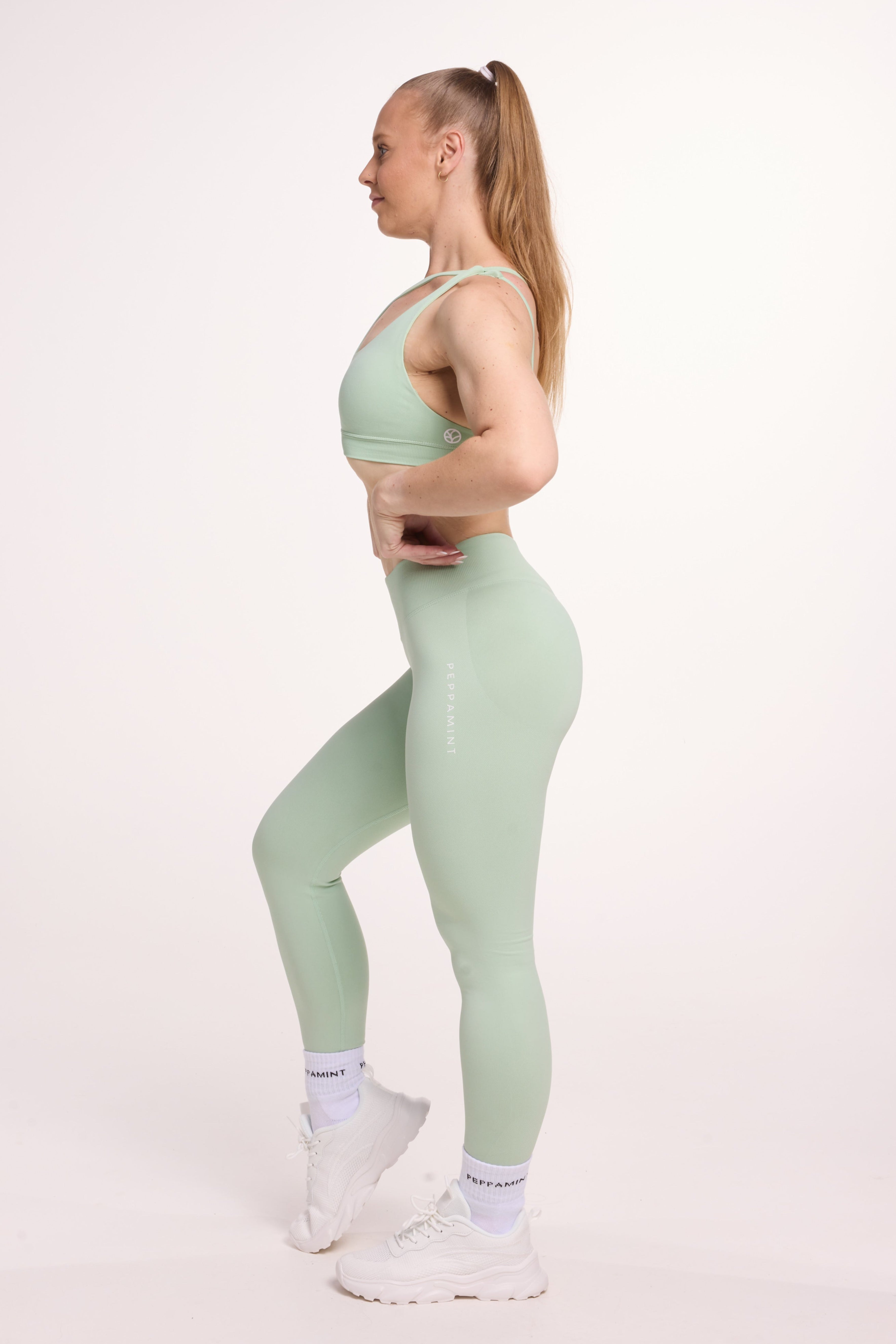 Front cross over strap activewear bra in seamless fabric with adjustable back straps, and ribbed supportive under bust band with seamless gym tights with booty contouring panels, invisible scrunch technology, sweetheart shaped back seams and thick supportive fabric in mist green