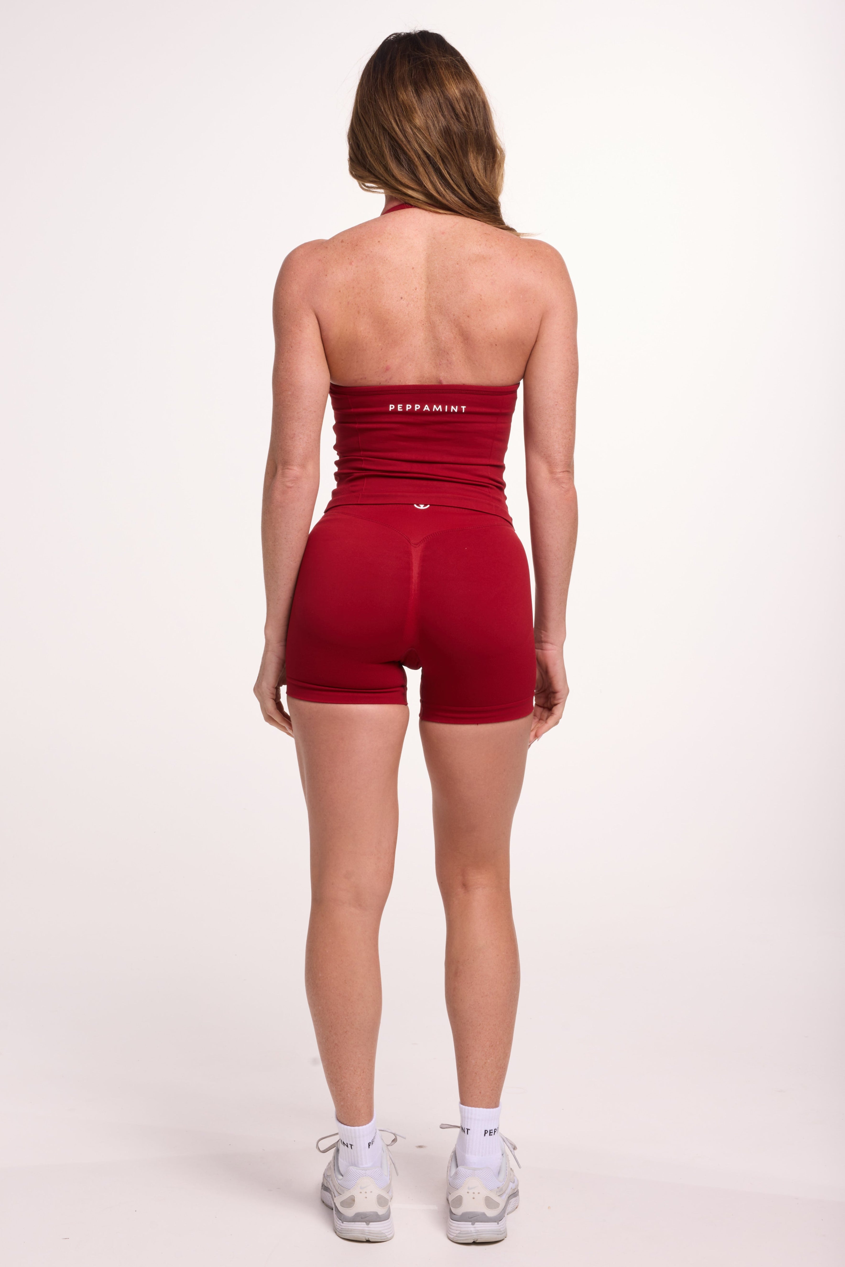 Halter neck tank top with breast contouring panels and a ruched front seam, a built in bra, and an open upper back design and seamless gym tights with booty contouring panels, invisible scrunch technology, sweetheart shaped back seams and thick supportive fabrics in cherry red