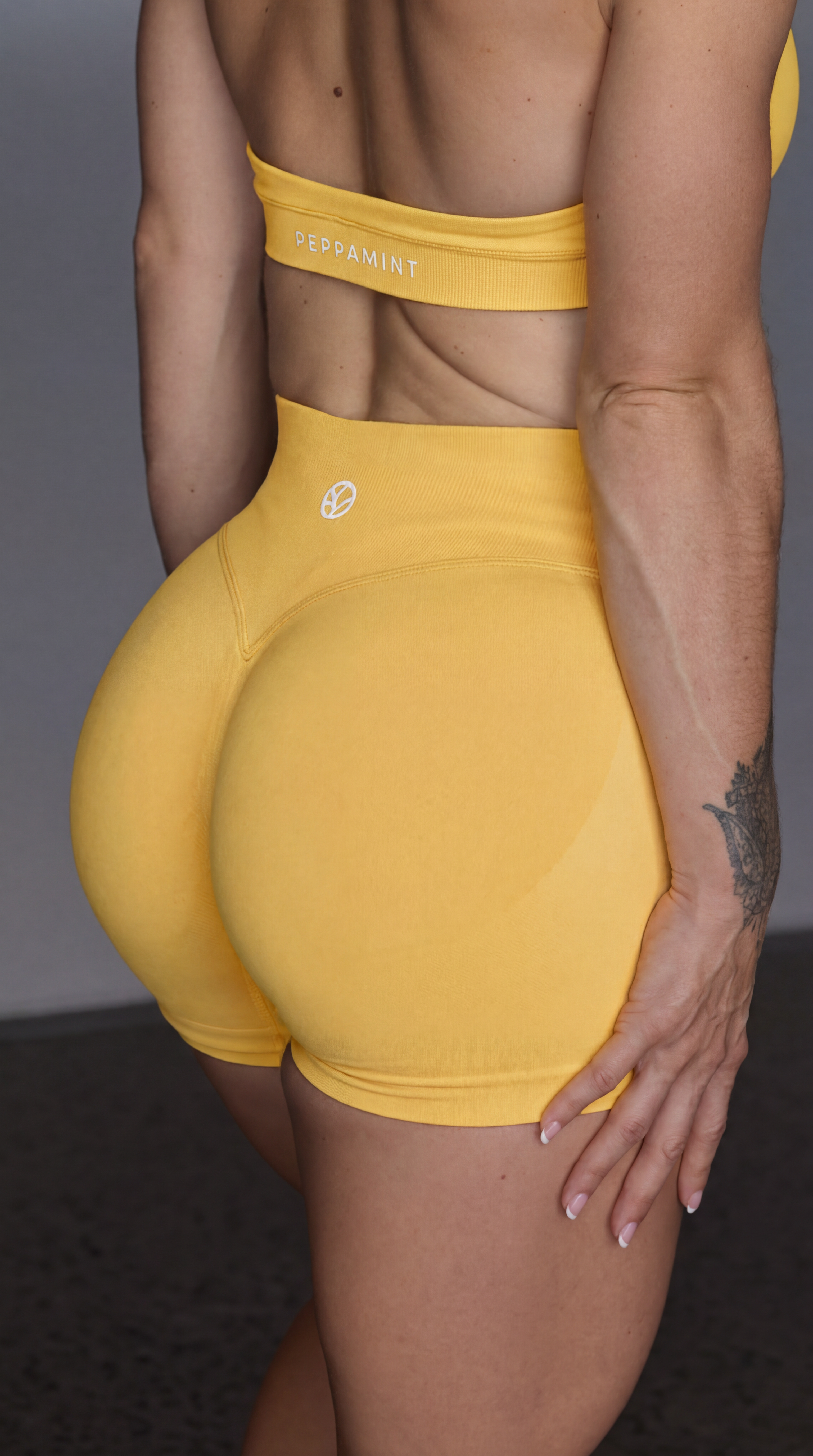 Person wearing mango sorbet booty enhancing shorts and sports bra with white brand logo on a dark background