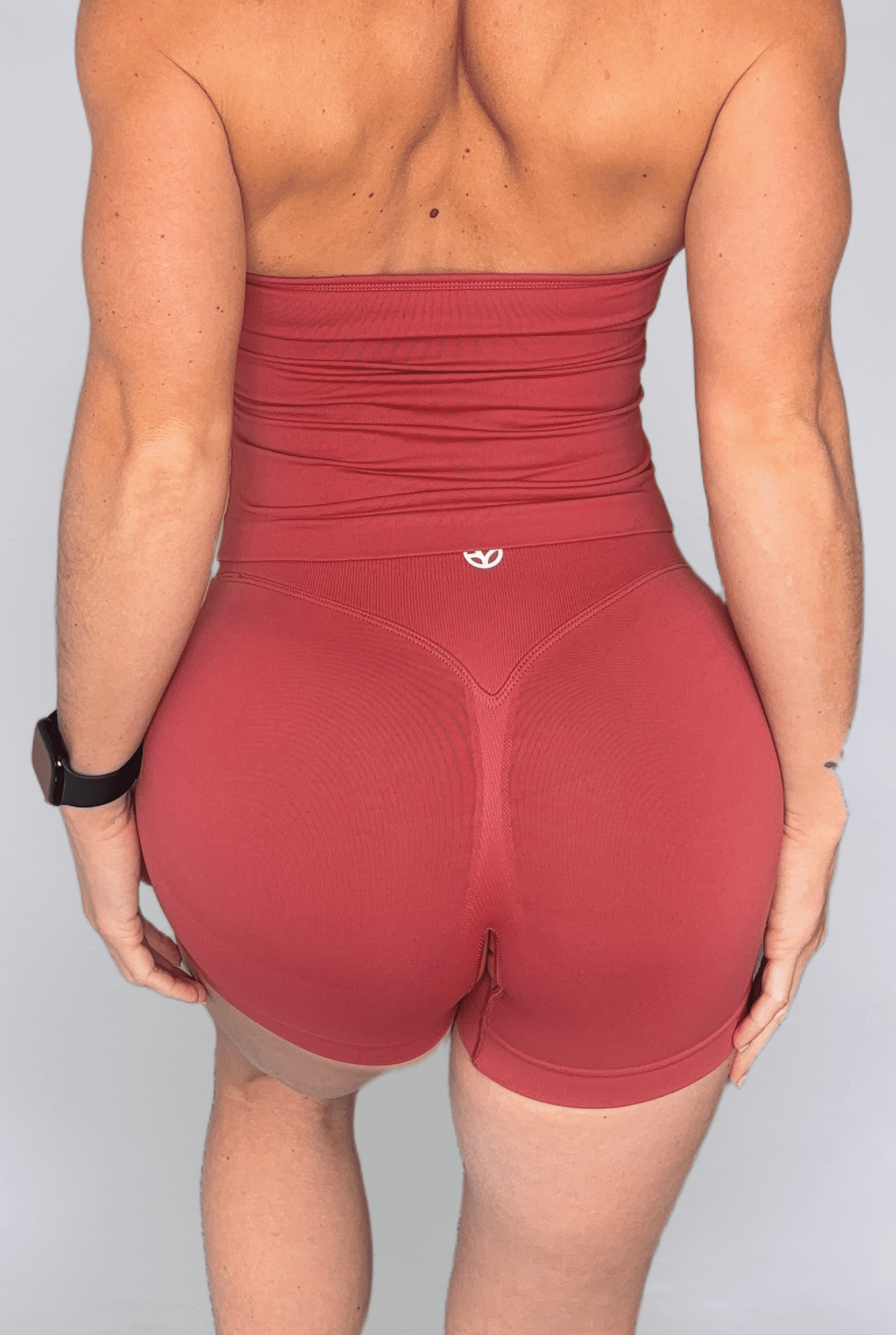 Rear view of a woman wearing high-waisted terracotta shorts featuring a small white logo on the back waistband.