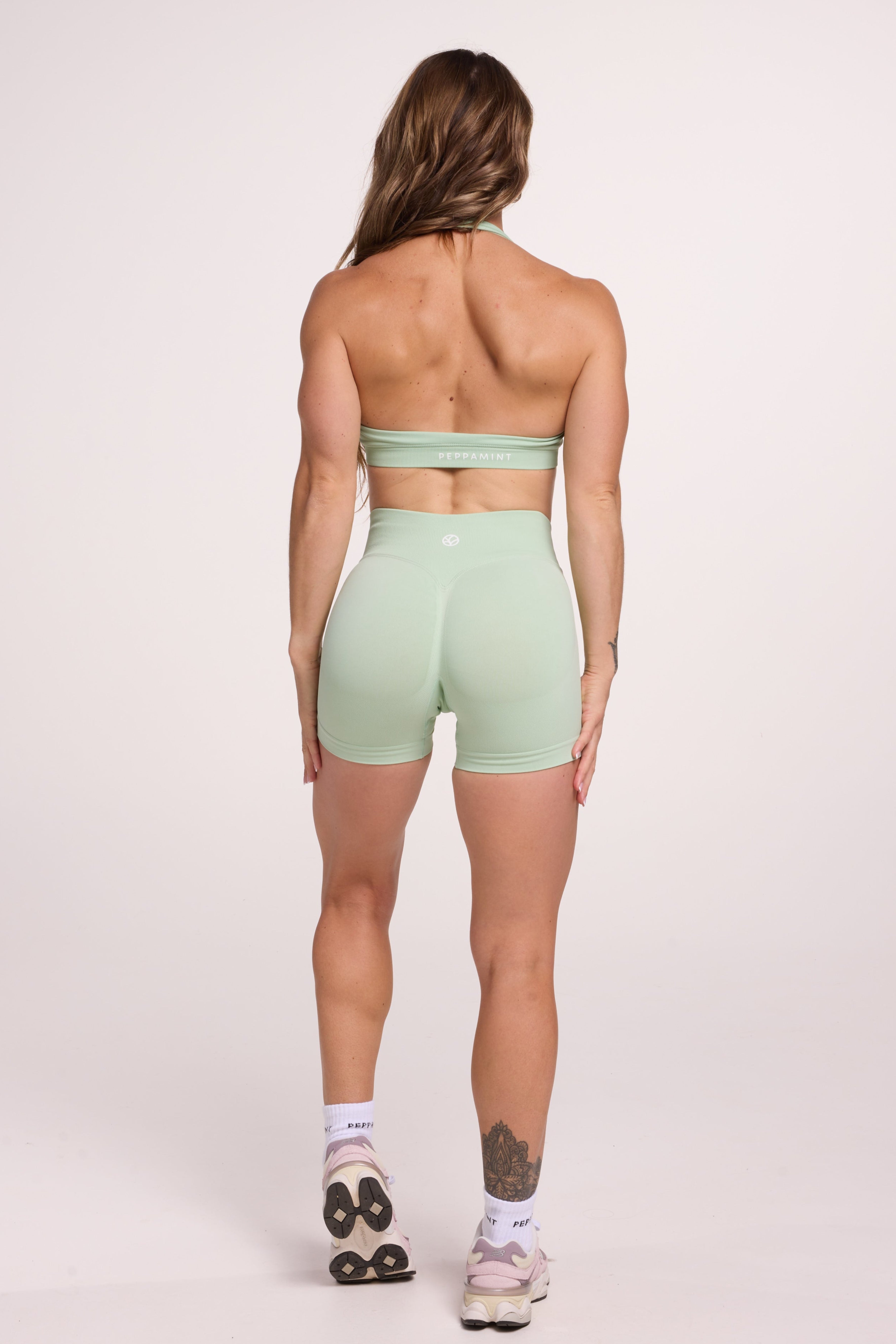 Seamless halter bra with a thick supportive fabric blend and a branded back strap, with a ribbed elastic hem and seamless gym shorts with booty contouring panels, invisible scrunch technology, sweetheart shaped back seams and thick supportive fabric in mist green